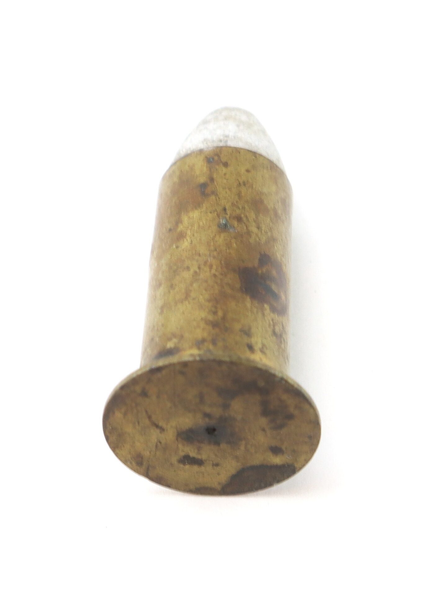 A close-up of an old, tarnished brass bullet casing with a lead tip, shown standing upright on a white background.