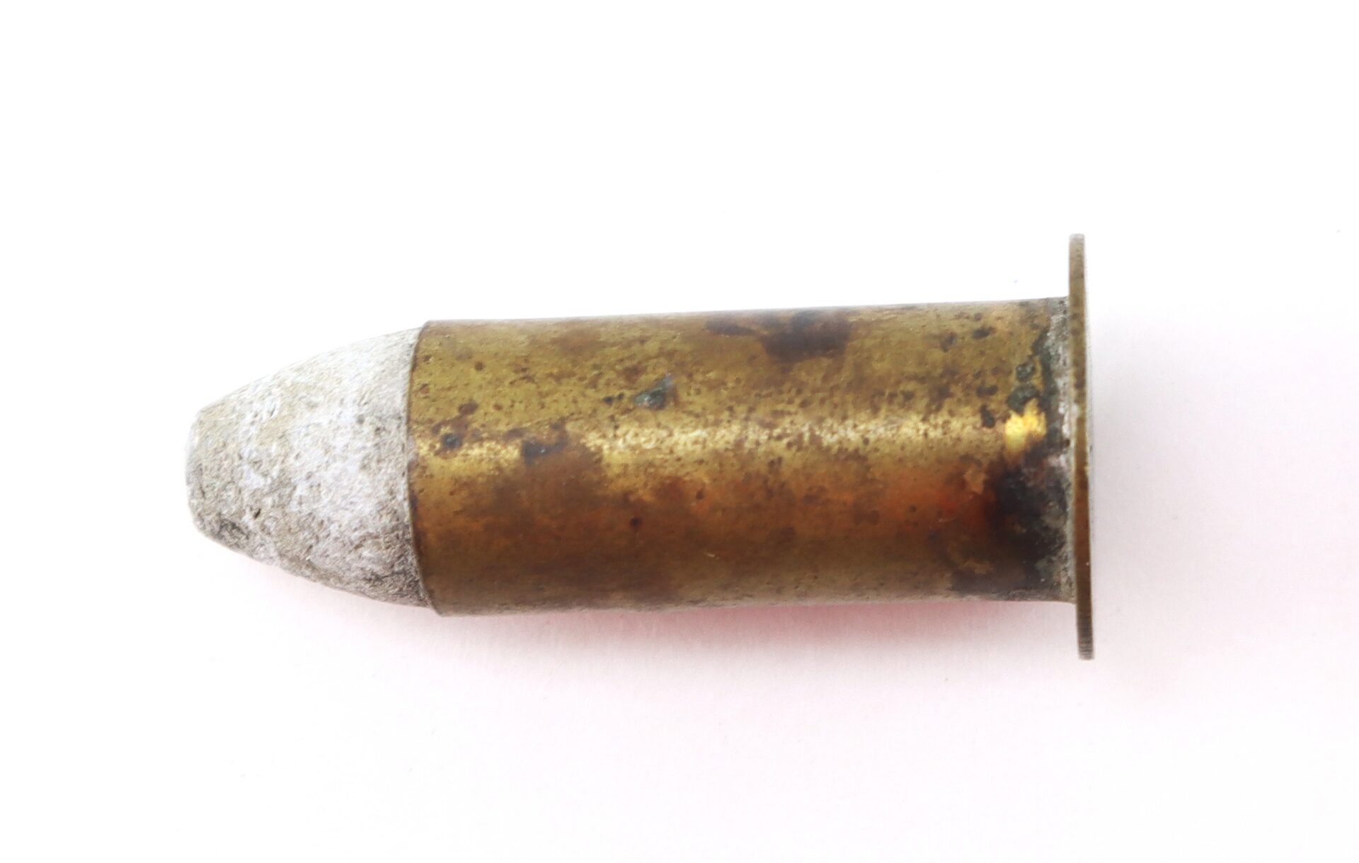 A tarnished and corroded brass bullet cartridge with a lead tip, lying on a white background.