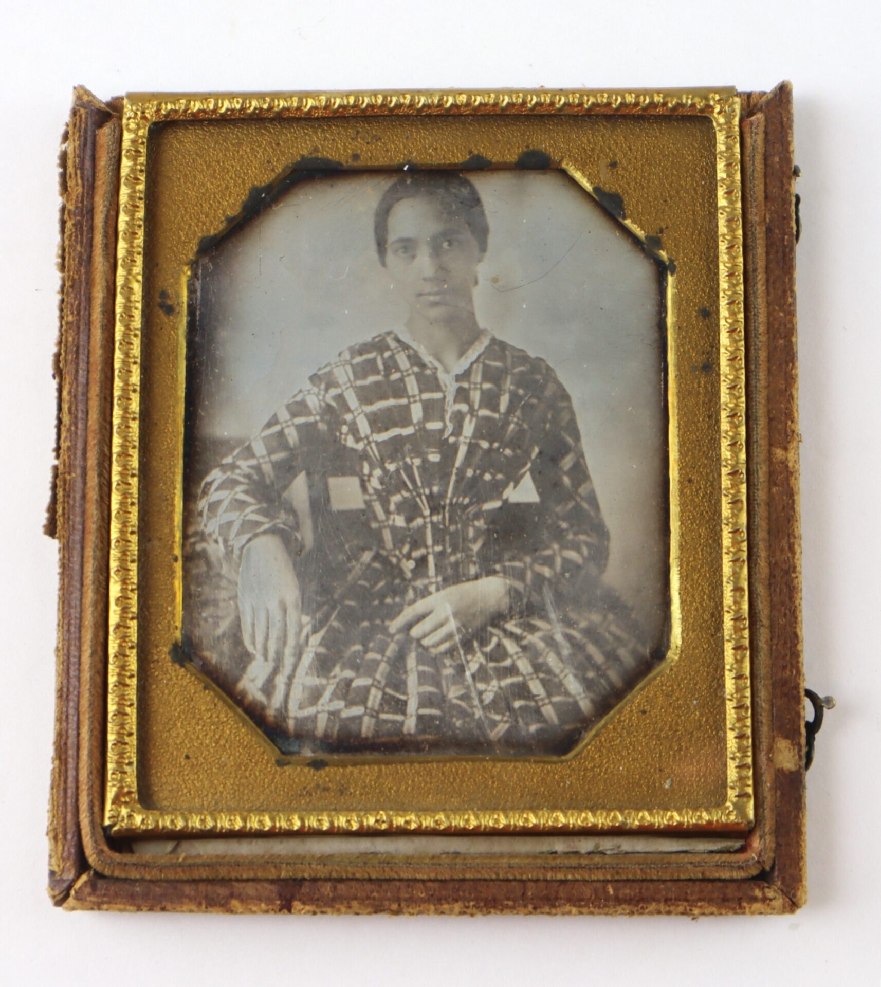 Sepia-toned portrait of a woman in a plaid dress, seated, framed in an ornate, vintage, gold-edged case.