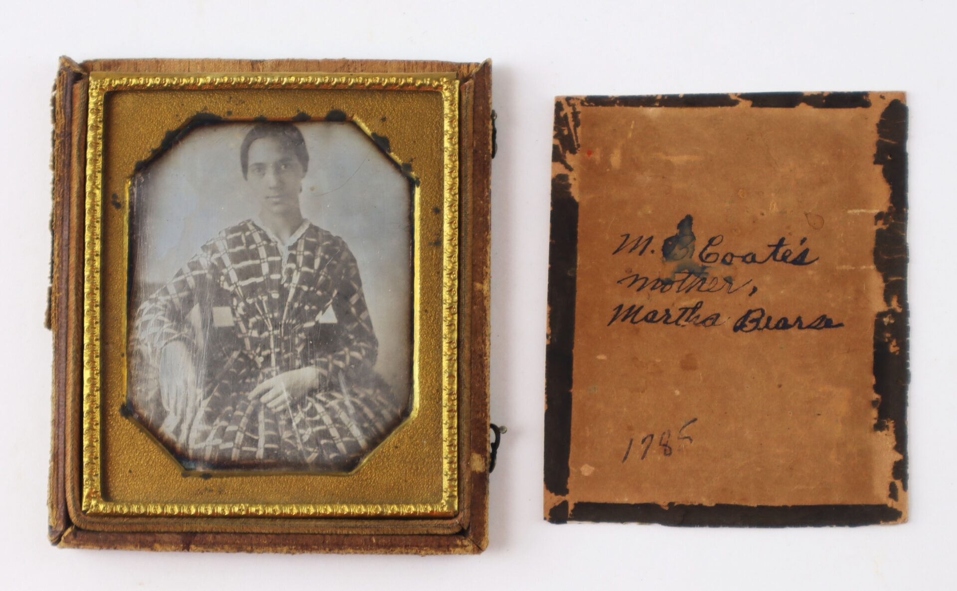 An old black-and-white portrait of a woman in patterned clothing in a vintage frame, next to a labeled card reading "M. E. Coates' mother, Martha Bura, 1865.