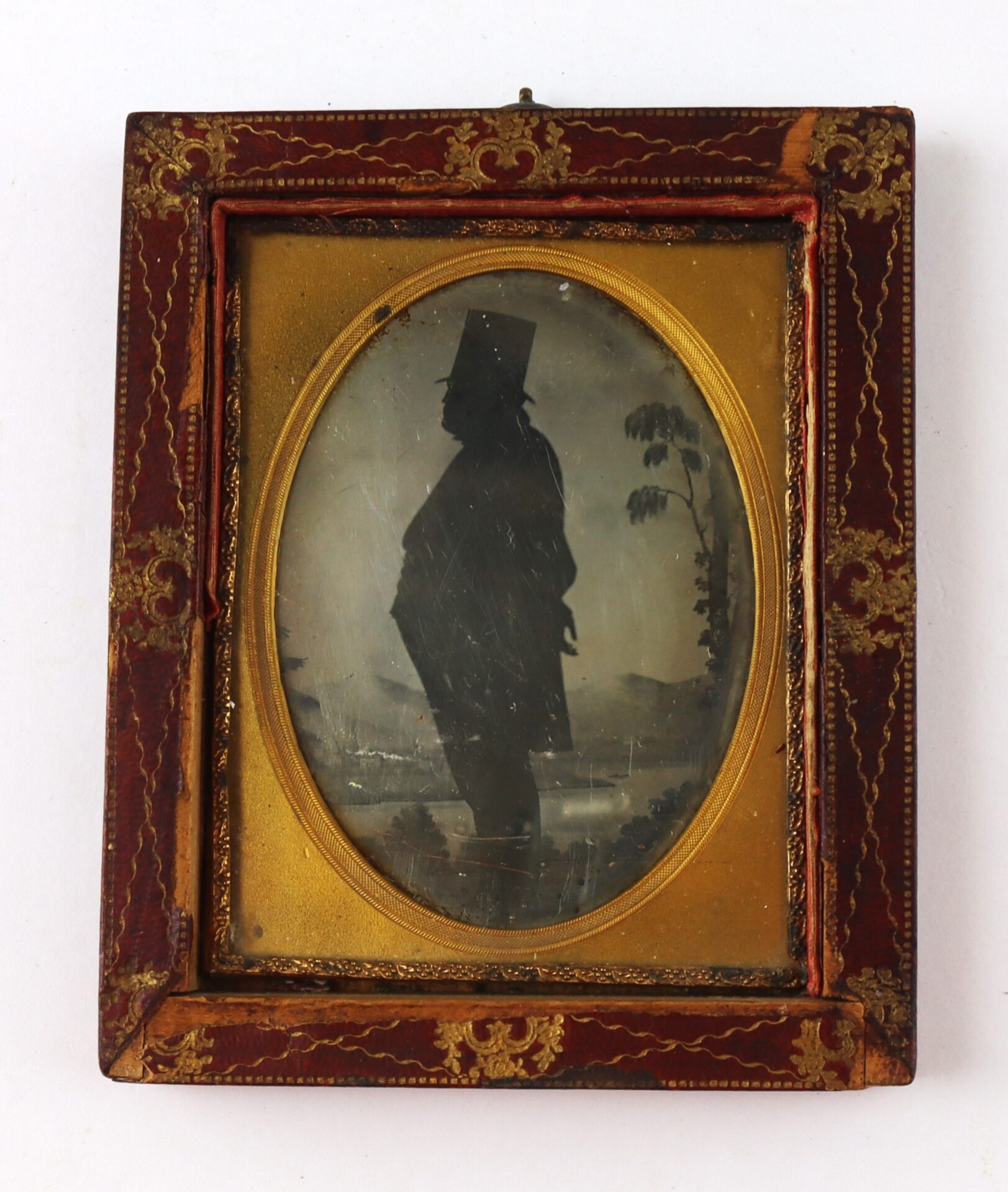 Framed oval silhouette portrait of a person in profile, wearing a top hat, set against a landscape background with a tree.