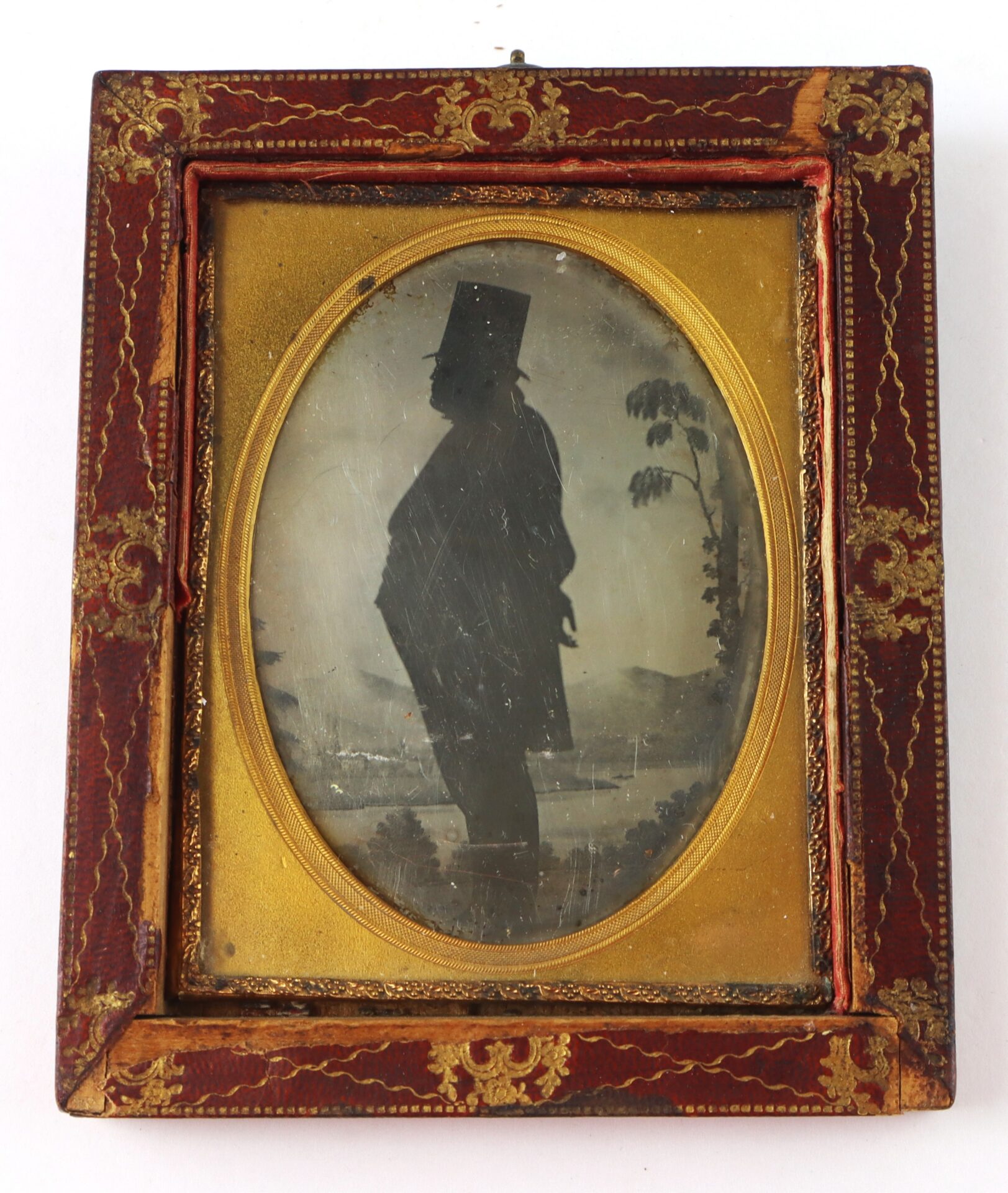 Photograph of an antique framed silhouette portrait of a man in profile, wearing a top hat, with a landscape background.