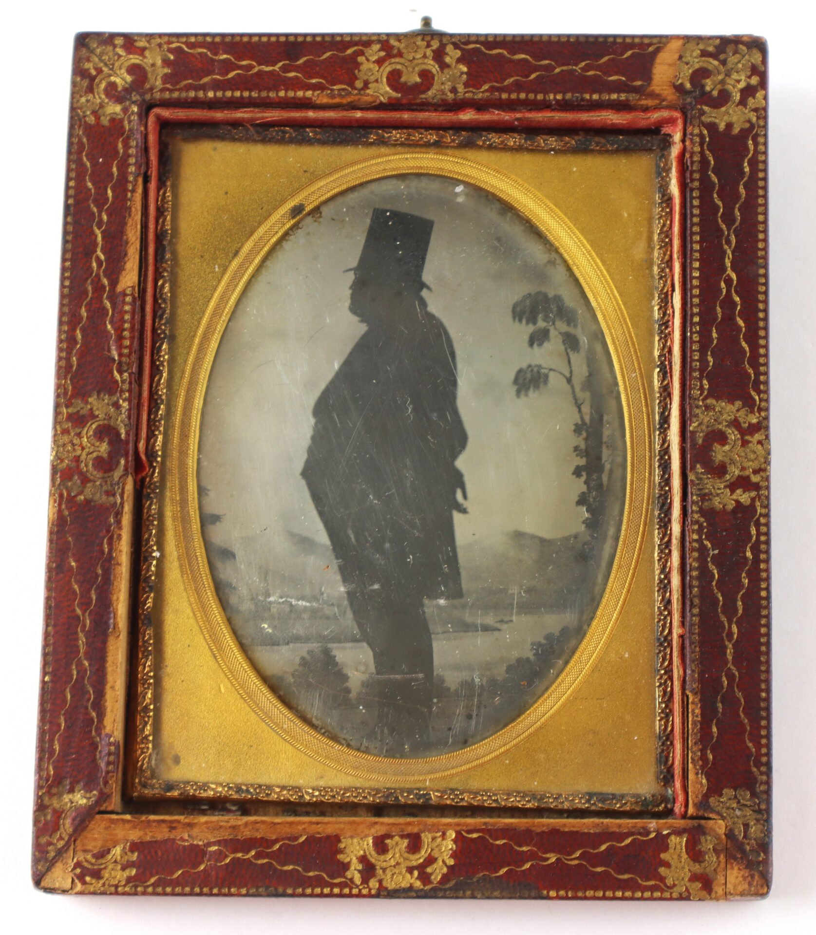 Old framed silhouette portrait of a man in profile, wearing a tall hat and coat, with a rural landscape background.