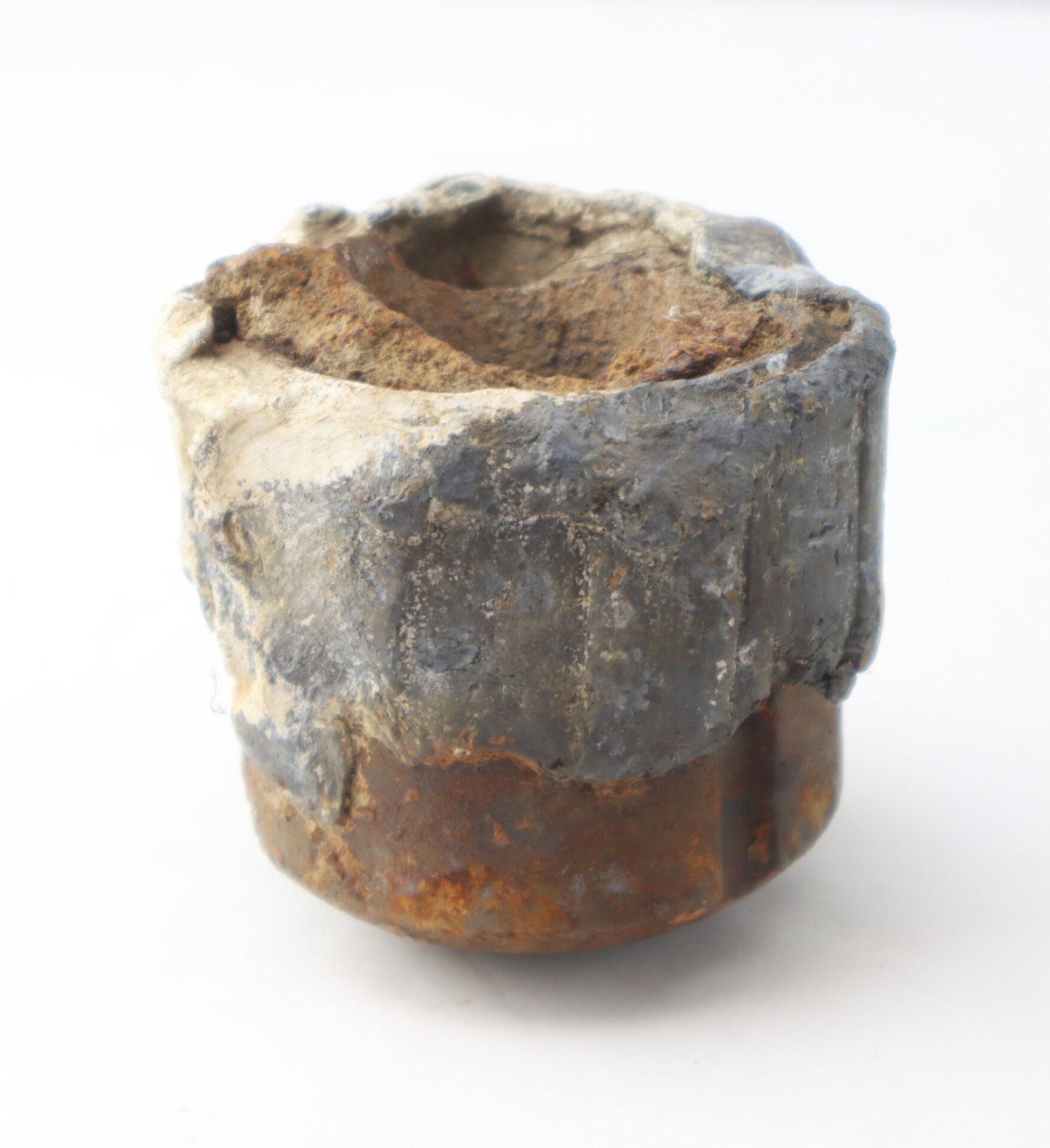 A close-up of a corroded, rusted metal and lead pipe cap against a plain white background.
