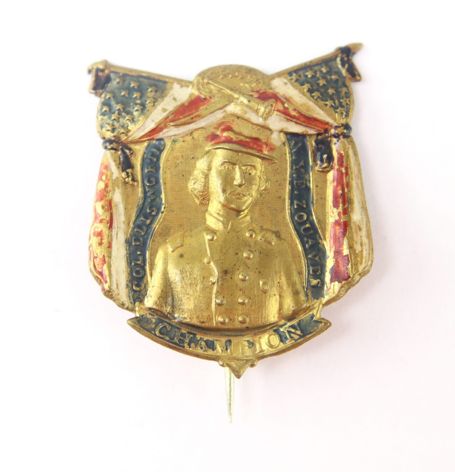 A vintage gold pin featuring a portrait of a uniformed figure, American flags, and the word "CHAMPION" at the bottom.