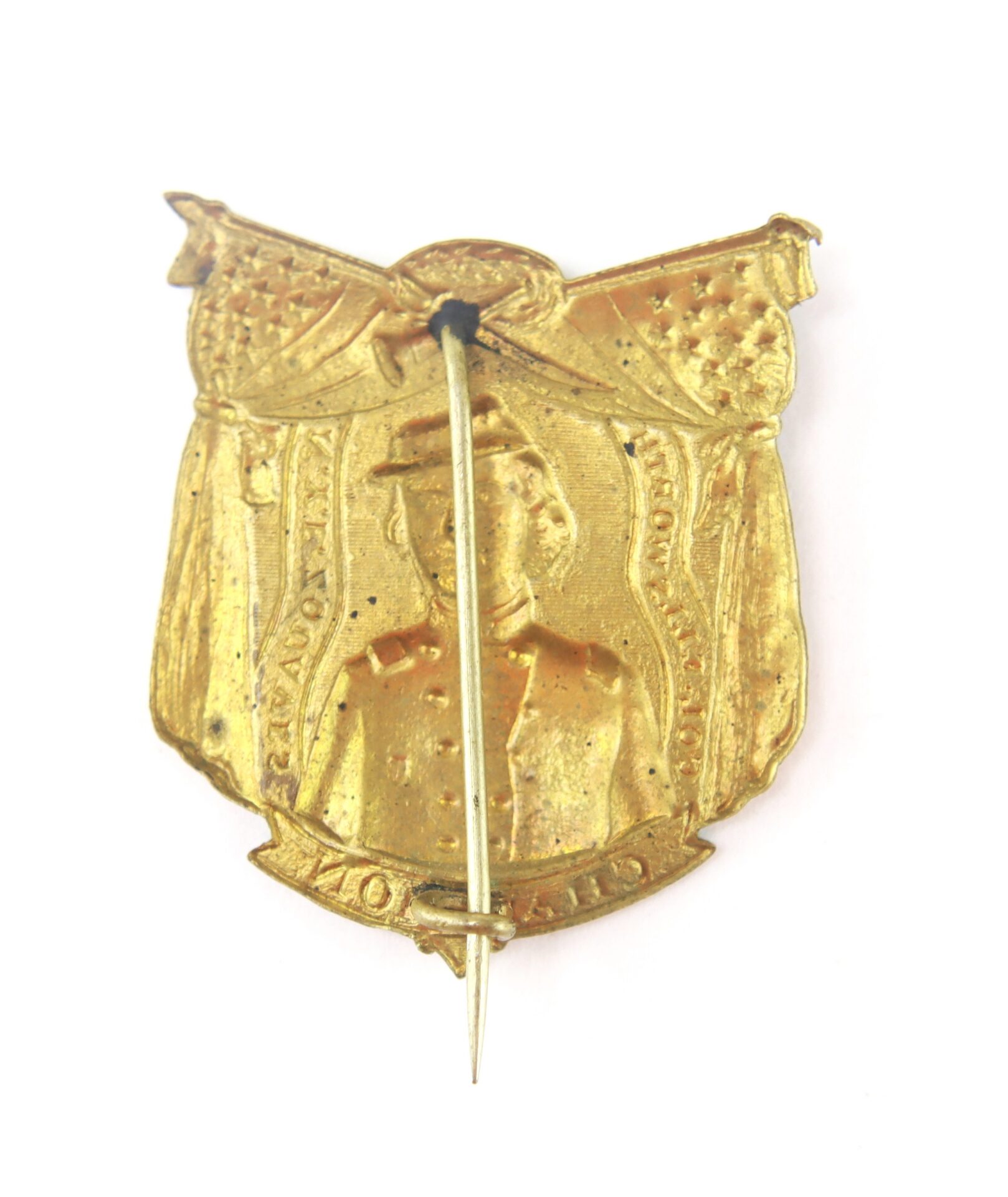 A gold-colored vintage pin featuring a raised portrait of a man in uniform beneath crossed flags, with a straight pin fastener on the back.