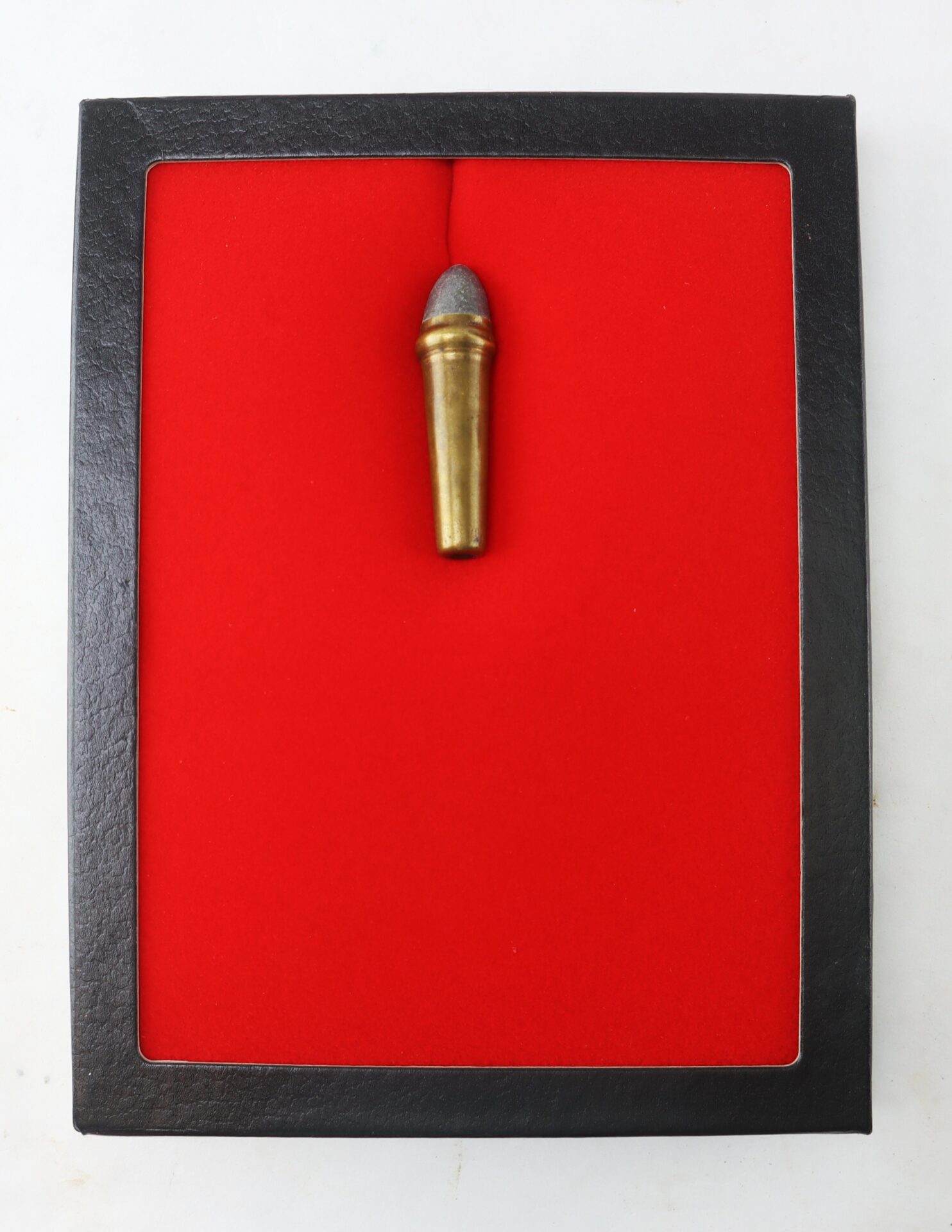 A single vintage bullet is displayed upright on a bright red background inside a black rectangular frame.
