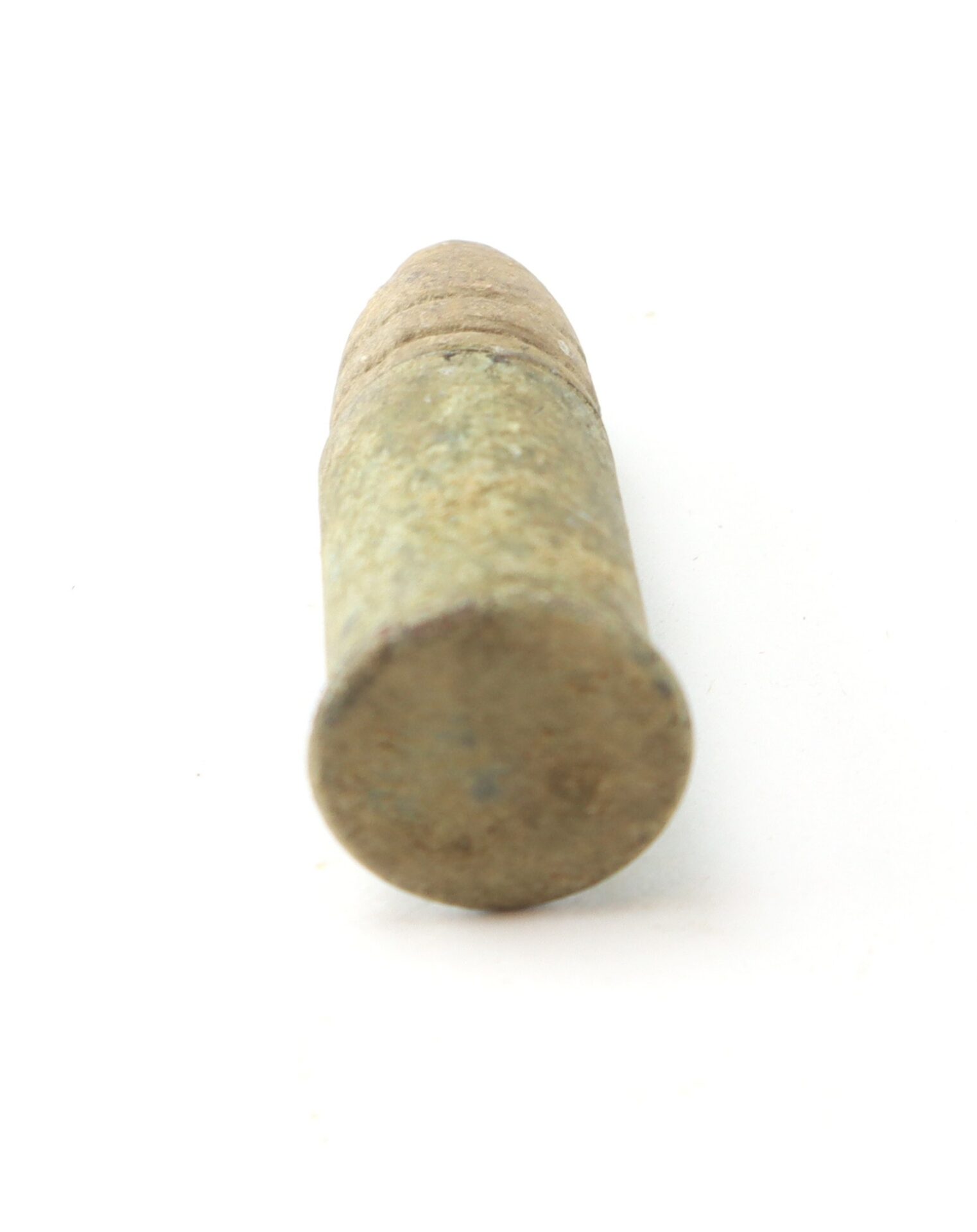 A close-up view of an old, weathered bullet lying on a white background, photographed from the base end.