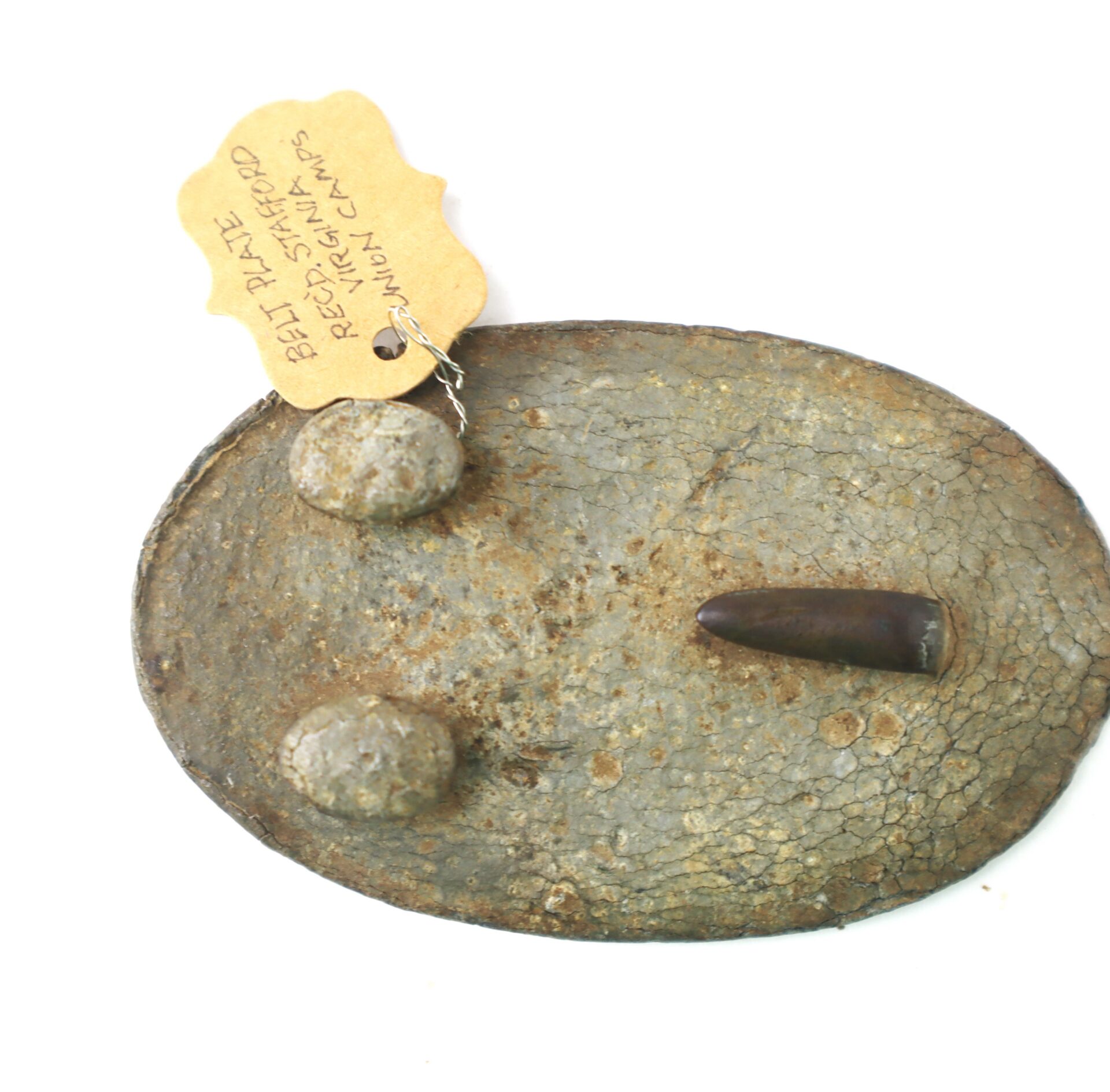 An oval-shaped metal belt plate with two round rivets and a dark protruding piece, attached to a tag labeled “Belt Plate, Red Star Camp, Junction Camp.”.