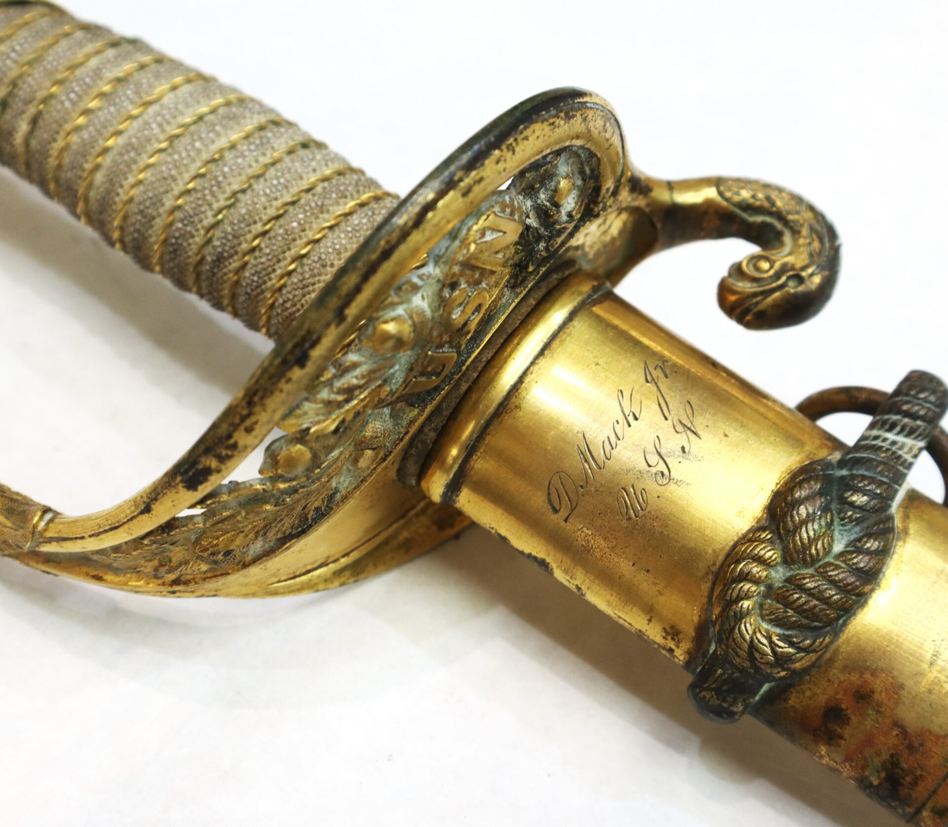 Close-up of an ornate gold sword hilt, inscribed with "USN" and "Dr. Mark Griffith, U.S.N.," featuring a coiled rope and snake design.
