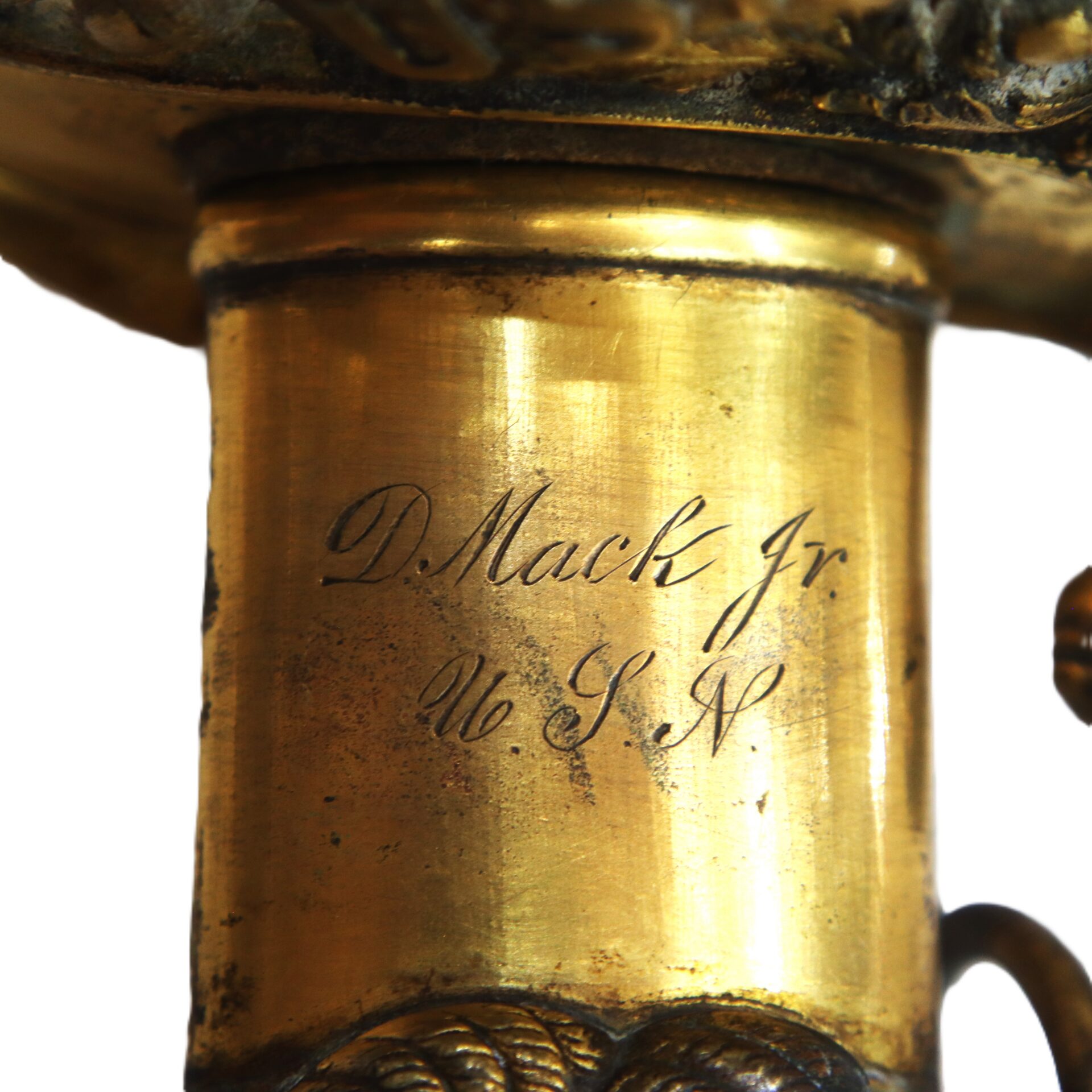 Close-up of an inscription on a brass object reading "D. Mack Jr U.S.N." in cursive lettering.