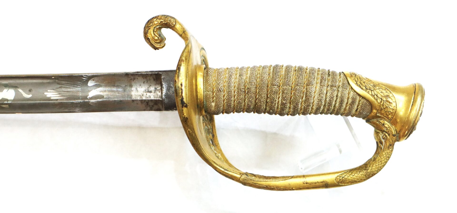 A close-up of an ornate sword hilt with a gold guard featuring an eagle design and a wrapped grip, alongside a partially visible engraved blade.