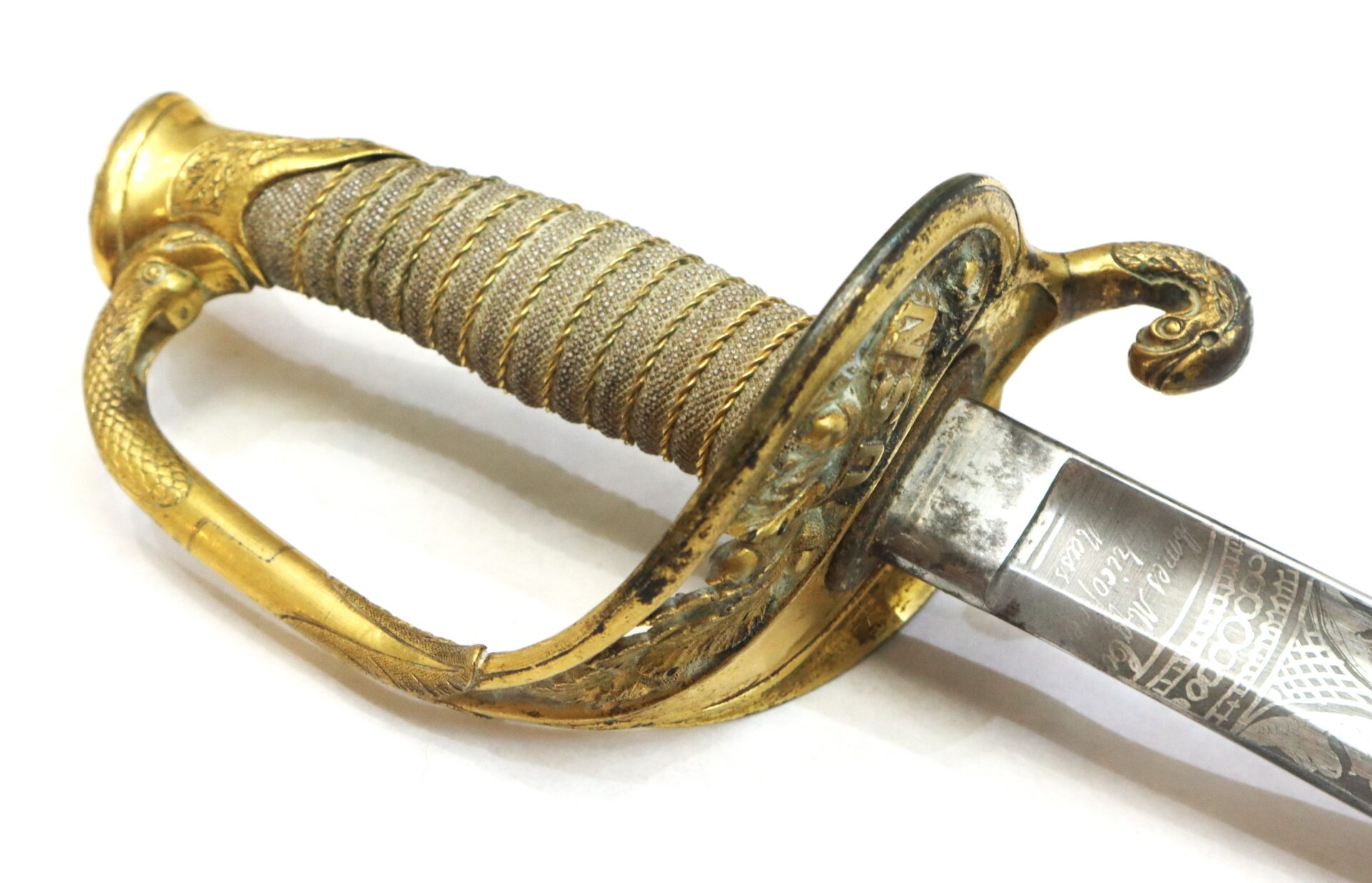 Close-up of an ornate sword hilt with a gold-colored handguard, textured grip, and part of a decorated steel blade.