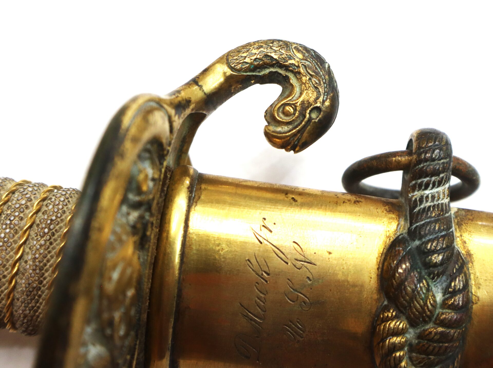Close-up of an ornate brass sword hilt featuring a decorative, sculpted animal head and engraved script on the blade’s base.