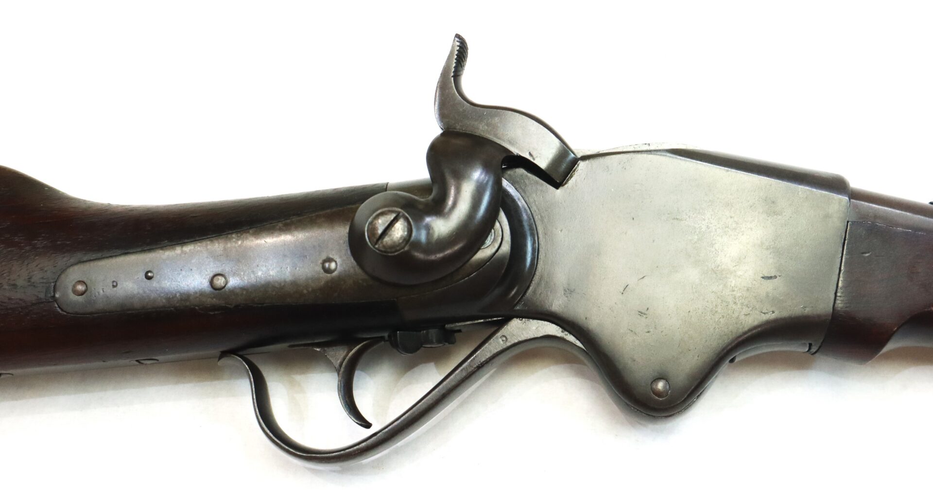 Close-up of the receiver, hammer, and trigger of an antique rifle with a dark wooden stock and metal components on a white background.