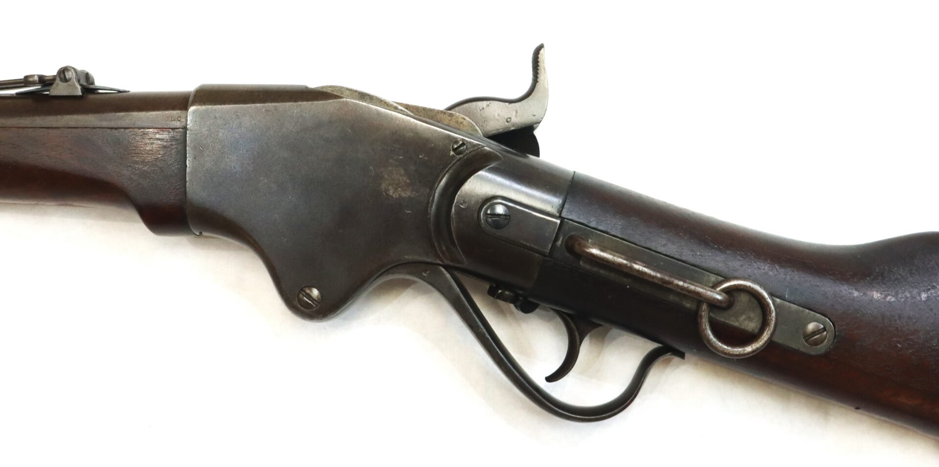 Close-up of an antique lever-action rifle showing the receiver, hammer, trigger, and part of the wooden stock against a white background.