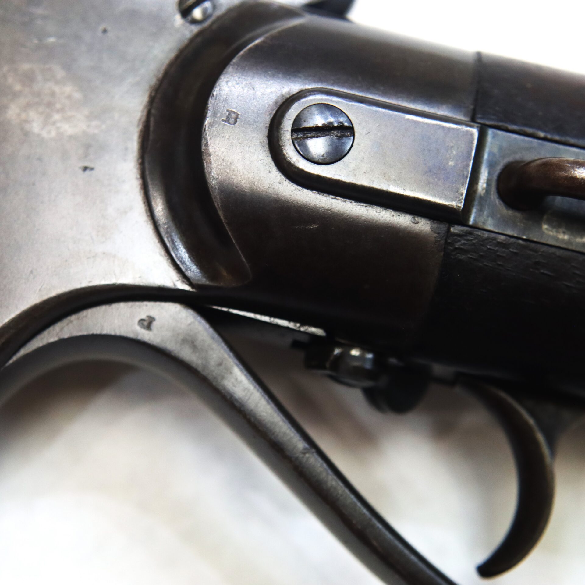 Close-up view of the metal trigger and part of the frame of an antique revolver, showing screws and surface details.