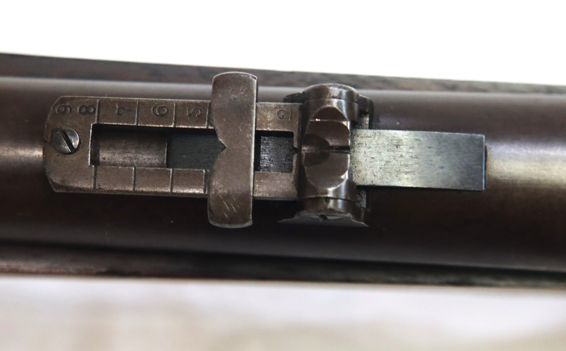 Close-up view of an adjustable rear sight mounted on the barrel of a rifle, showing distance markings and metal components.