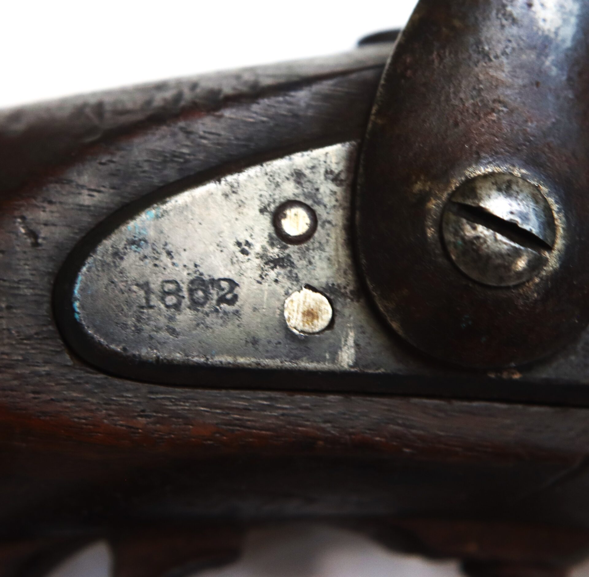 Close-up of a metal plate on a wooden firearm, engraved with the number "1802" and secured by a large screw.