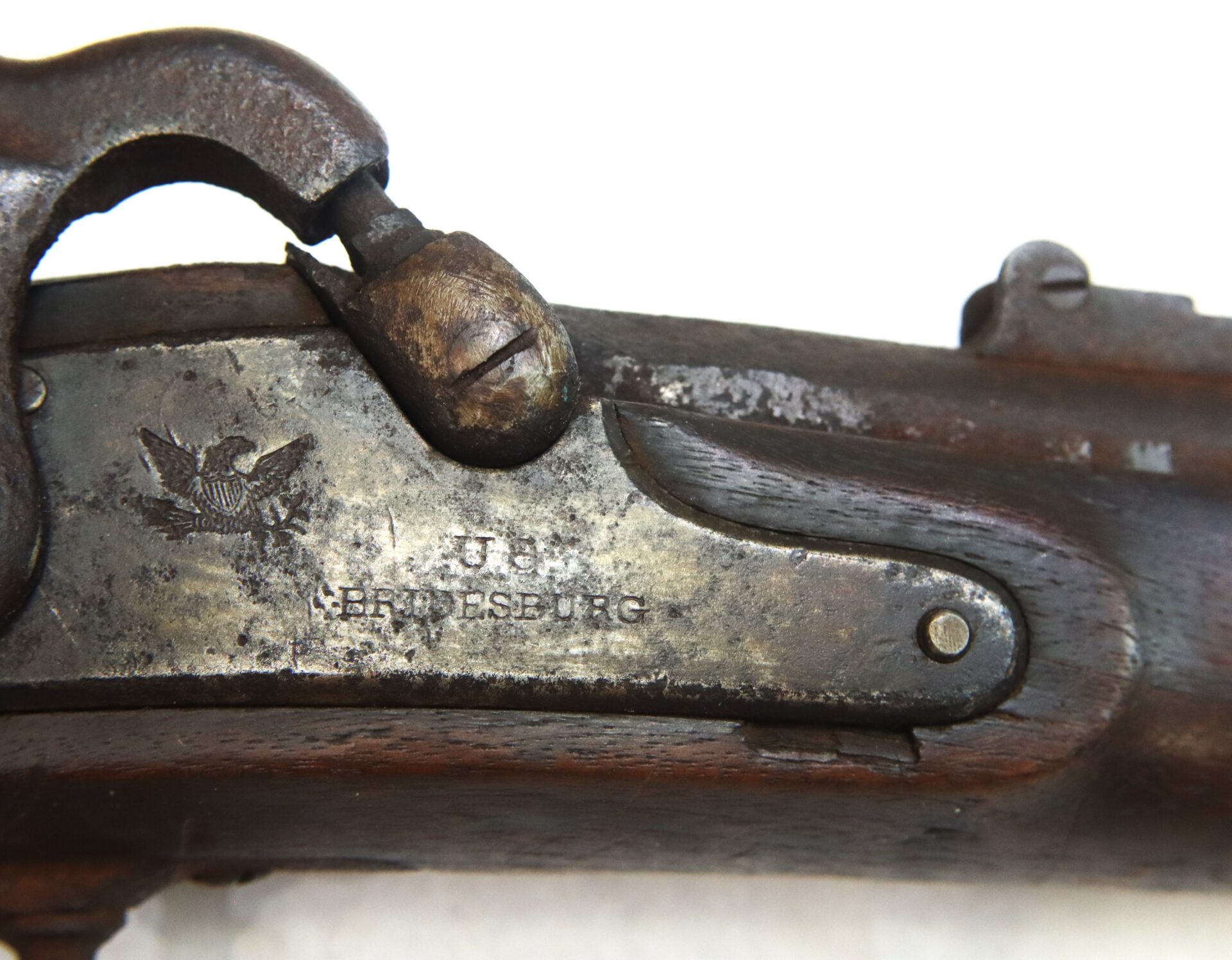 Close-up of a metal plate on an antique firearm, showing an engraved eagle emblem and the text "U.S. SPRINGFIELD," with visible signs of rust and wear.