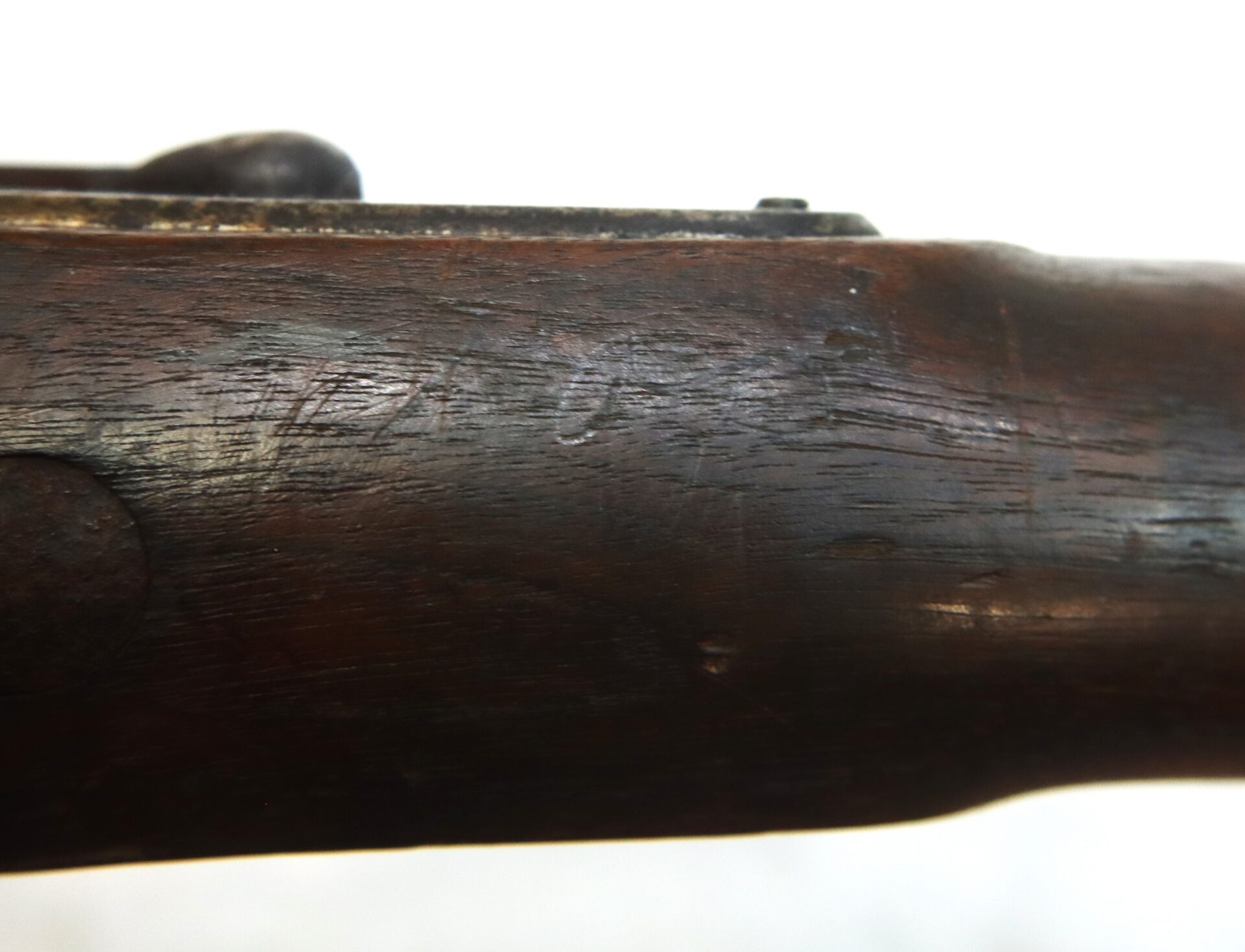Close-up view of a wooden rifle stock showing surface scratches, dents, and worn areas.