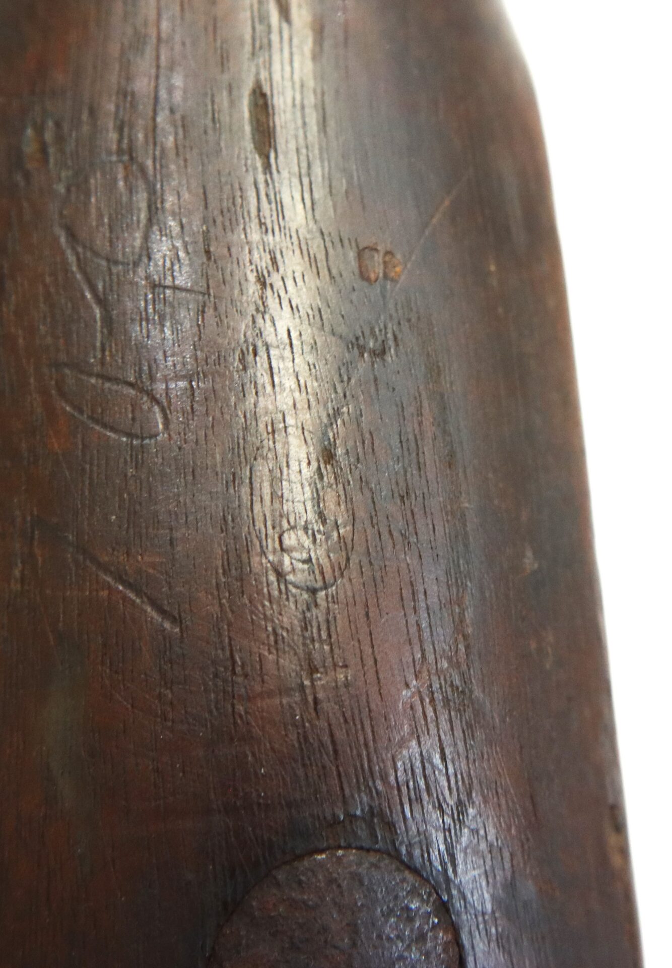 Close-up of a wooden surface with visible grain and faint carved markings, including a simple face and other unclear symbols.