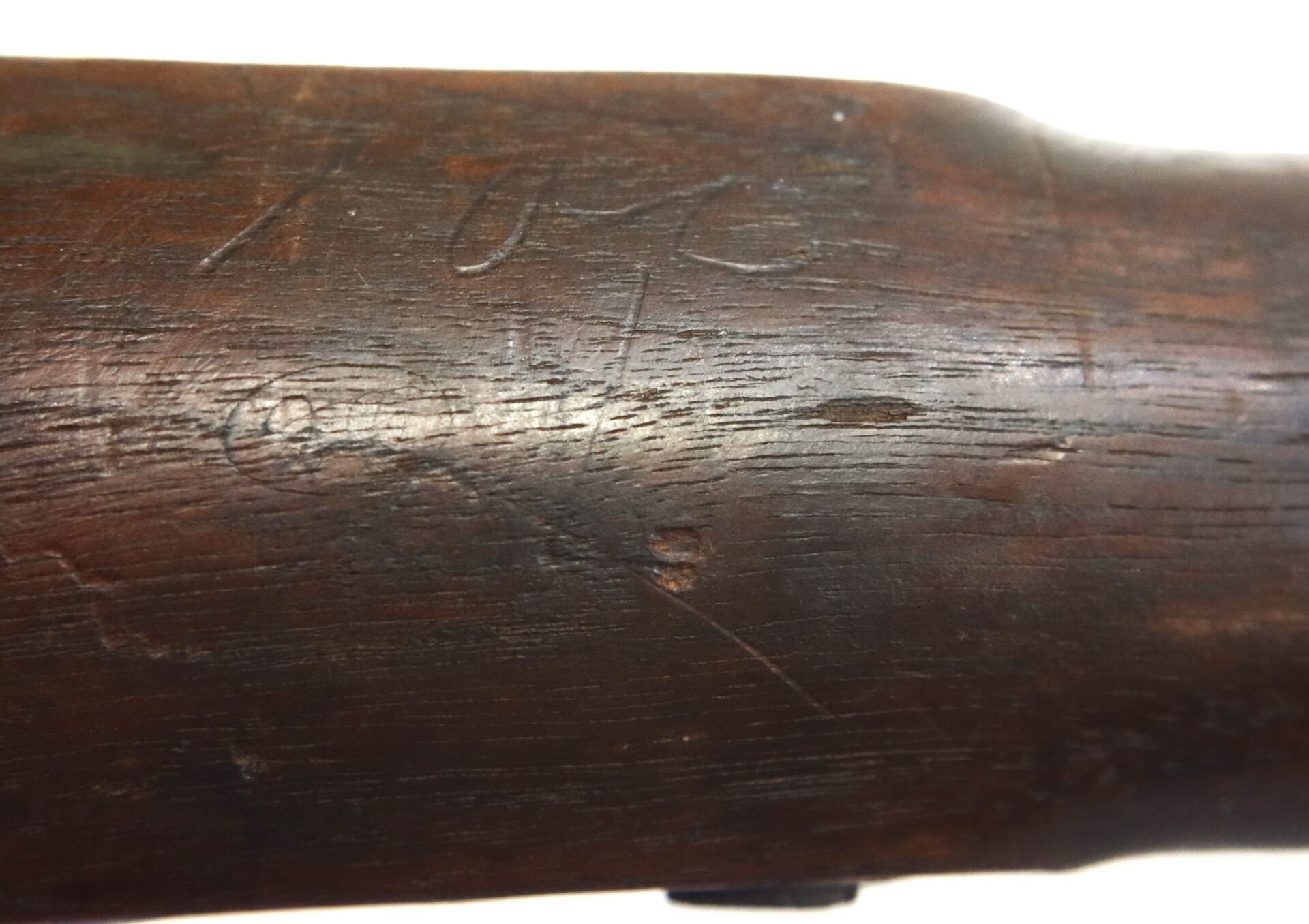Close-up of a wooden rifle stock with faint, worn engravings and scratches visible on the surface.