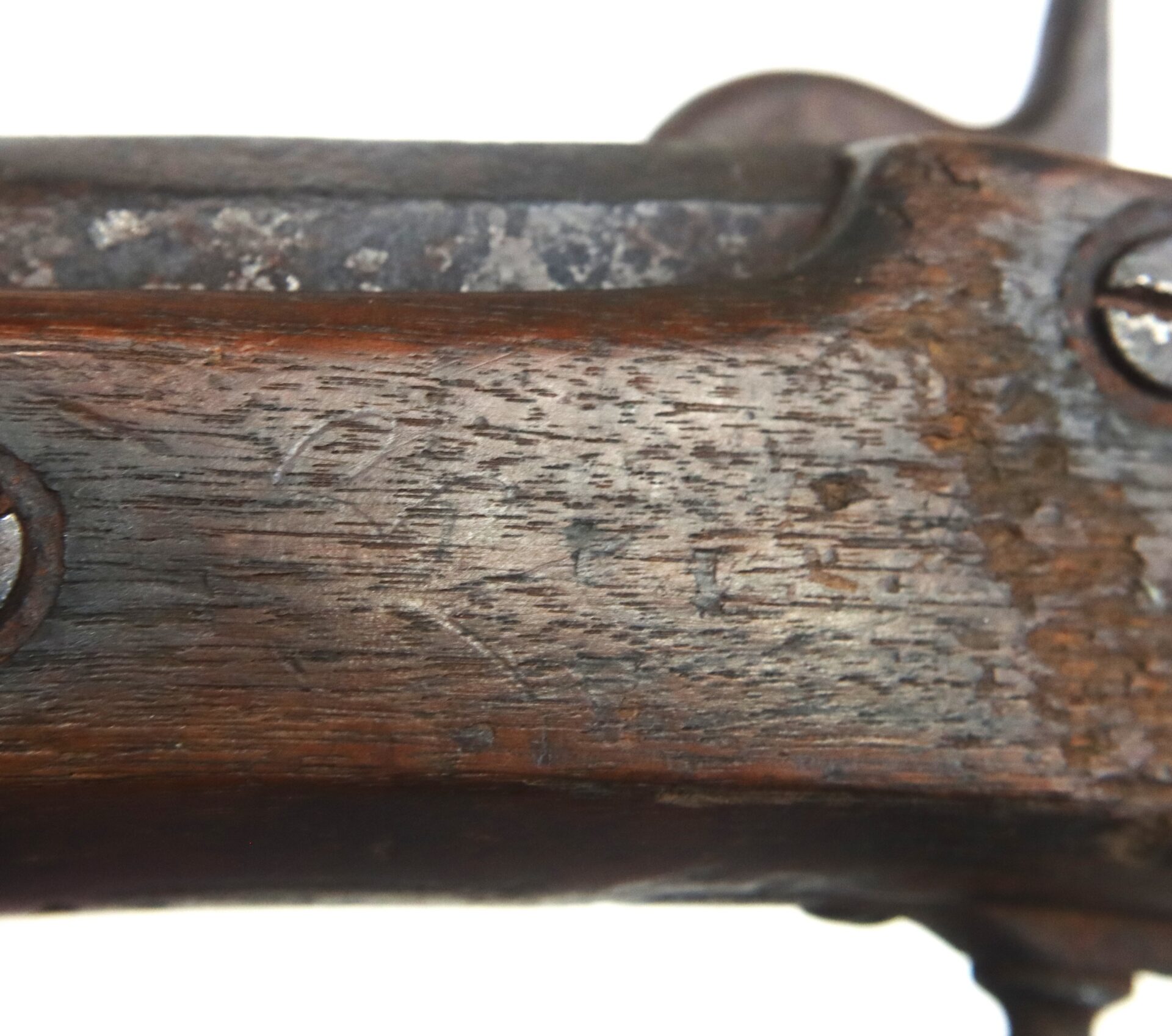 Close-up view of a weathered wooden rifle stock with visible scratches, metal screws, and signs of wear.