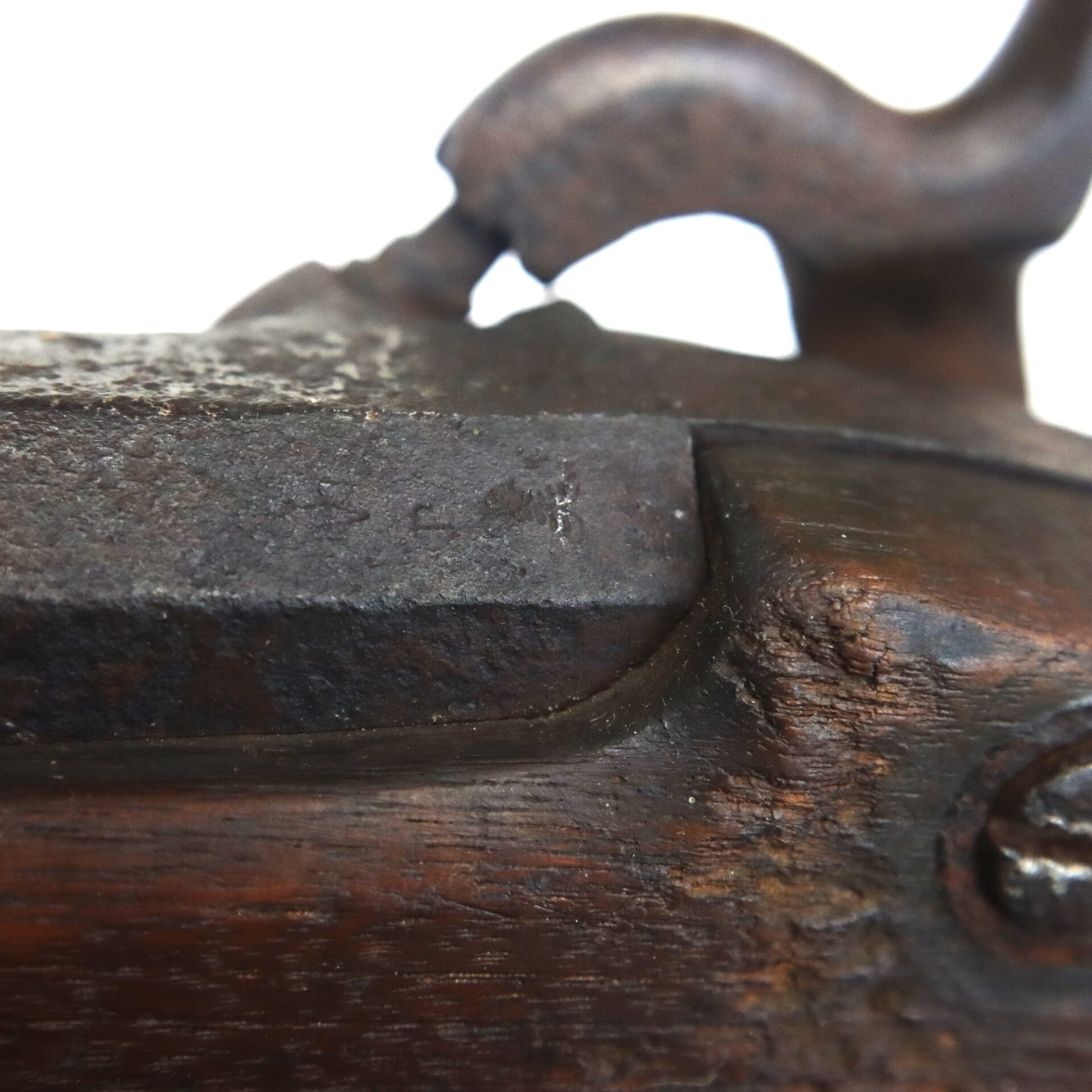 Close-up of a weathered, antique firearm lock mechanism made of dark metal and wood, showing signs of age and wear.