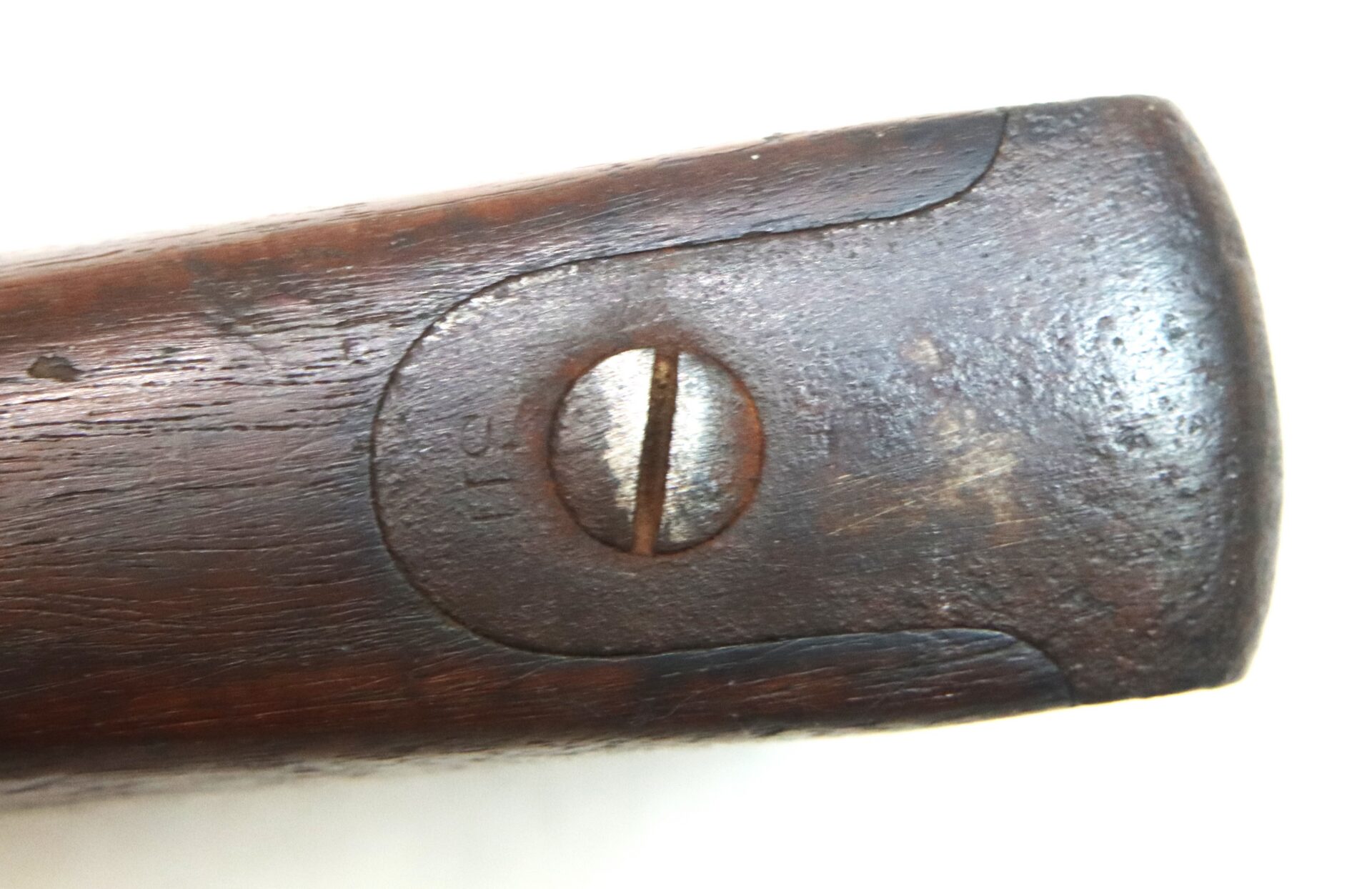 Close-up of a worn, wooden rifle buttplate with a single flathead screw in the center.