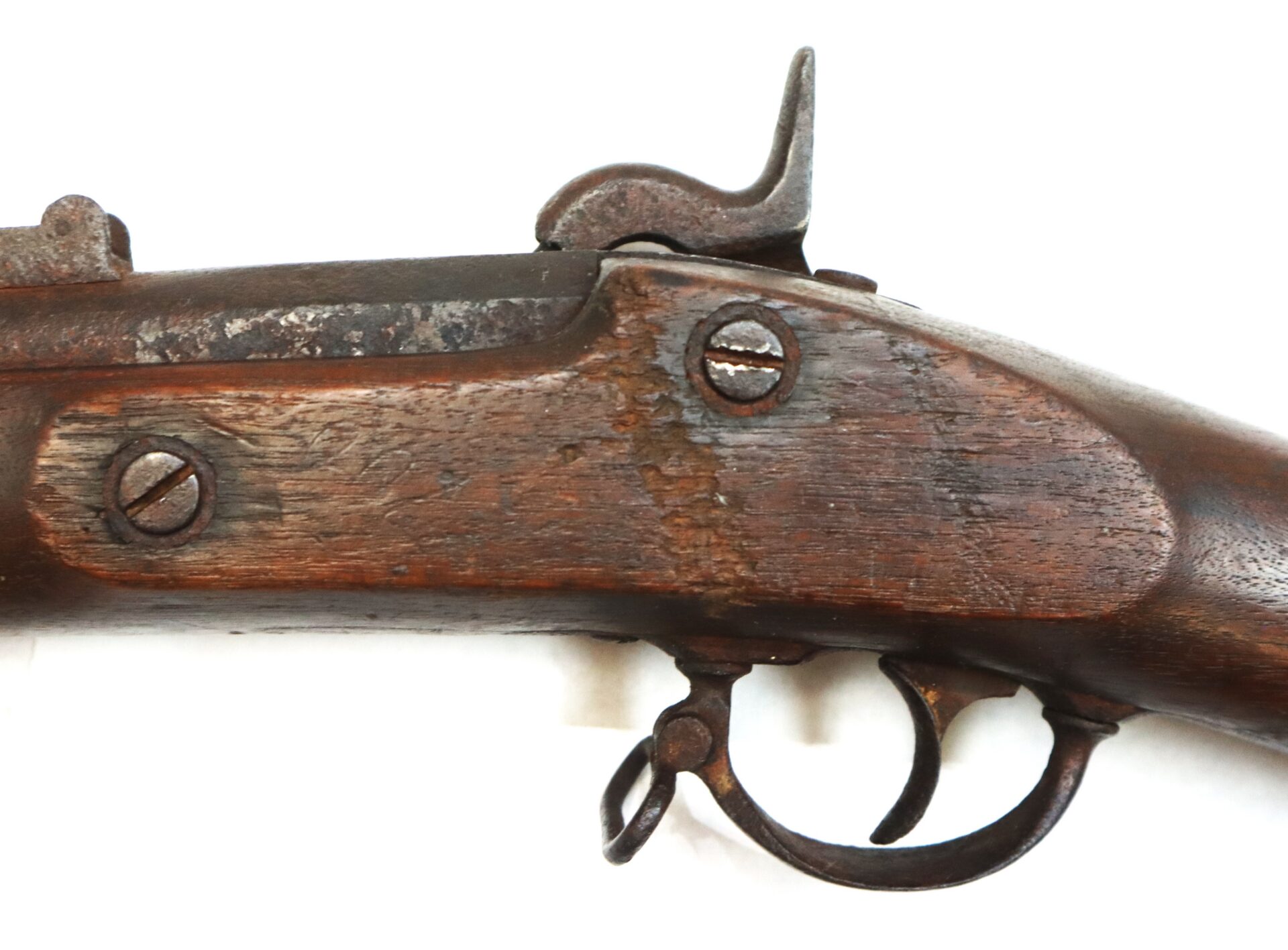 Close-up view of the lock and trigger area of an old, weathered flintlock or percussion rifle with a wooden stock and metal components.