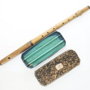 A wooden flute with finger holes is shown next to an open blue and green lined case and a closed, brown marbled outer case.