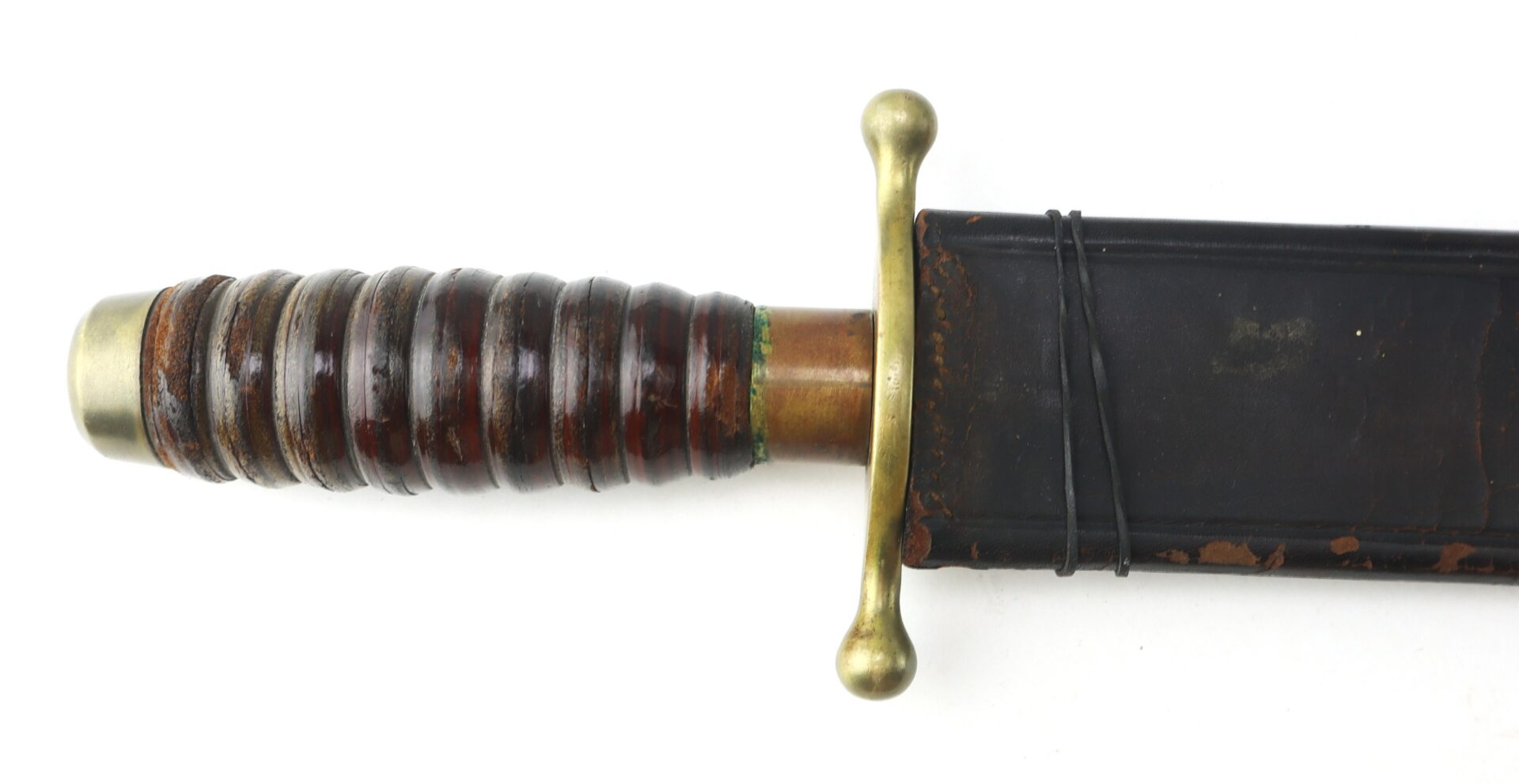 Close-up of a sword handle with a brass crossguard and rounded pommel, featuring a grooved wooden grip and partially visible black scabbard.