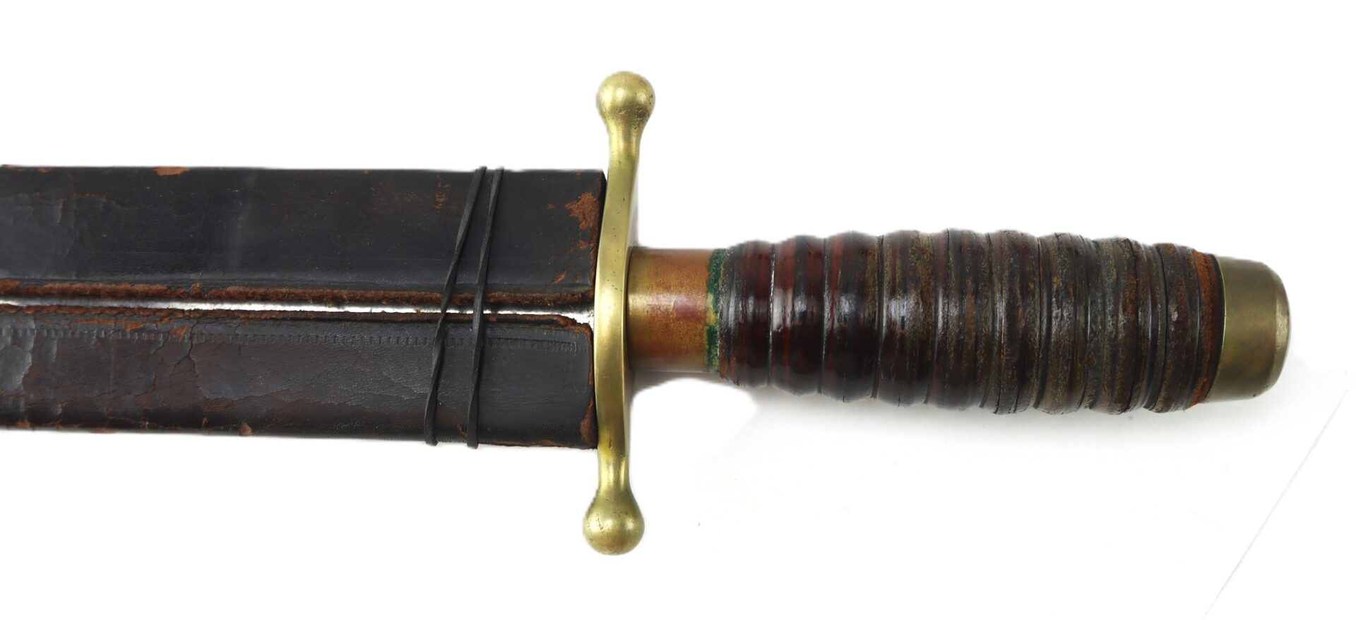Close-up of the hilt and part of the scabbard of a vintage short sword or dagger with a ribbed handle and brass guard.