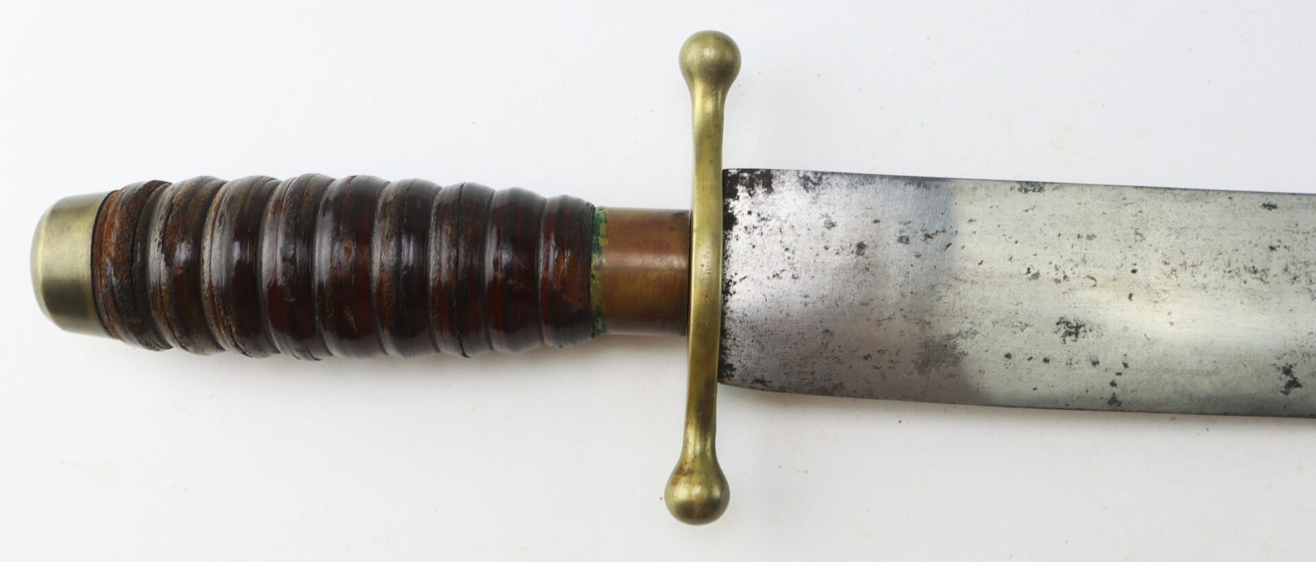Close-up of a vintage sword showing a ridged, dark handle with brass accents and a straight, double-sided blade with minor rust spots.