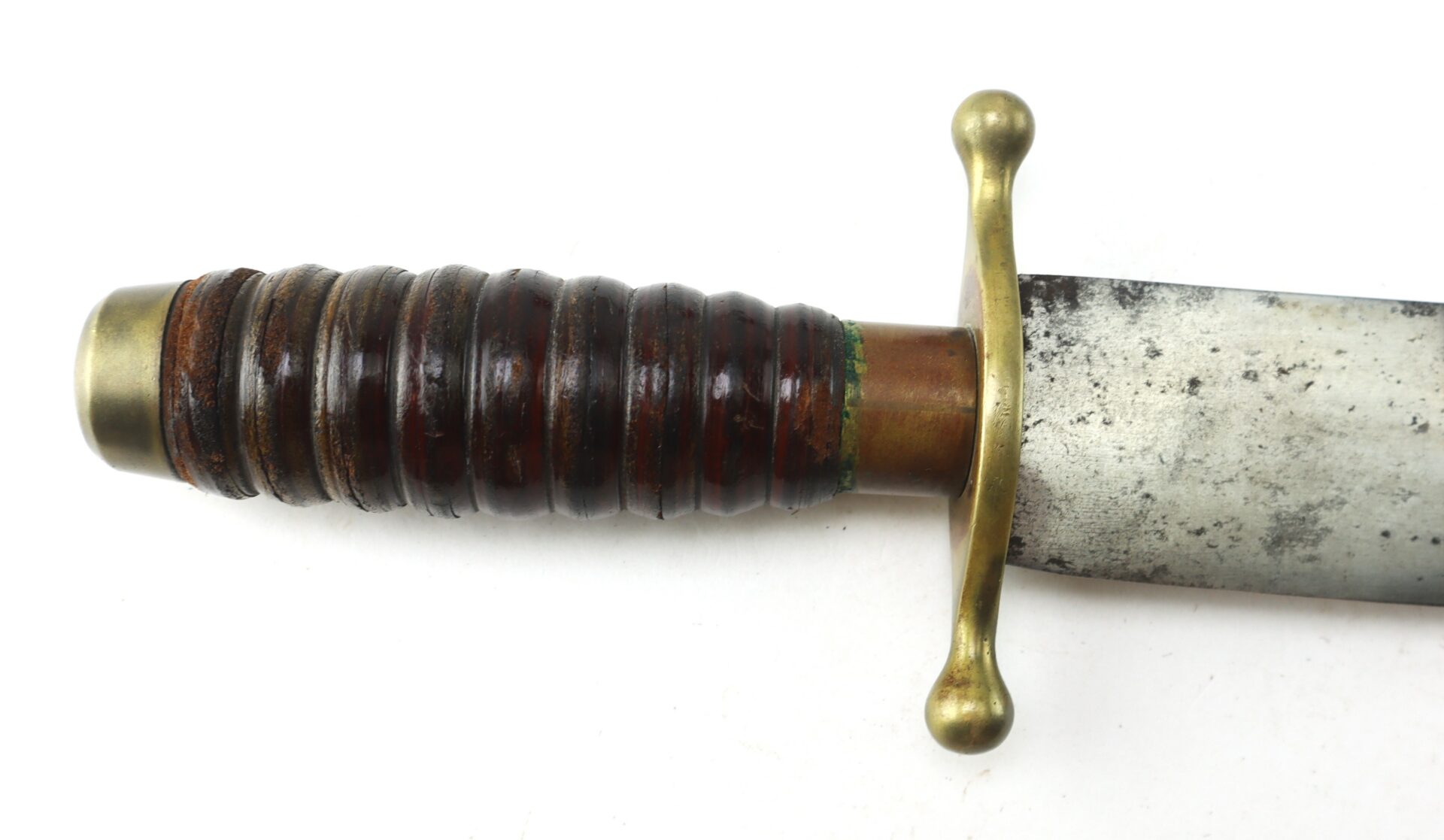 Close-up of a vintage sword handle with a grooved, dark brown grip, brass guard and pommel, and part of a tarnished blade.