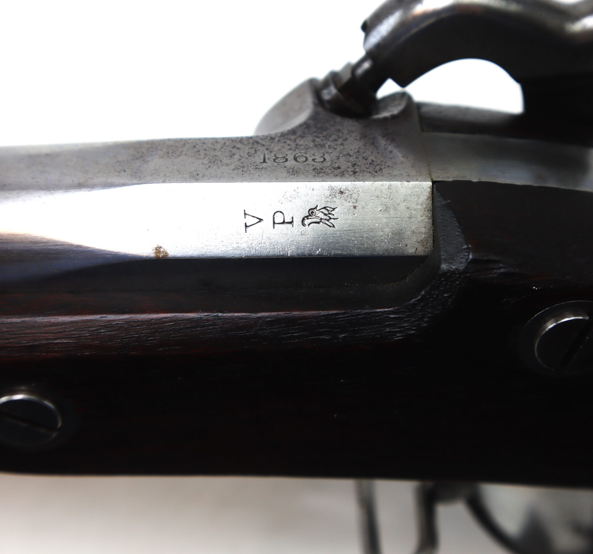 Close-up of a metal rifle receiver showing engraved markings, including the numbers "1863," a "V," a "P," and an eagle symbol.