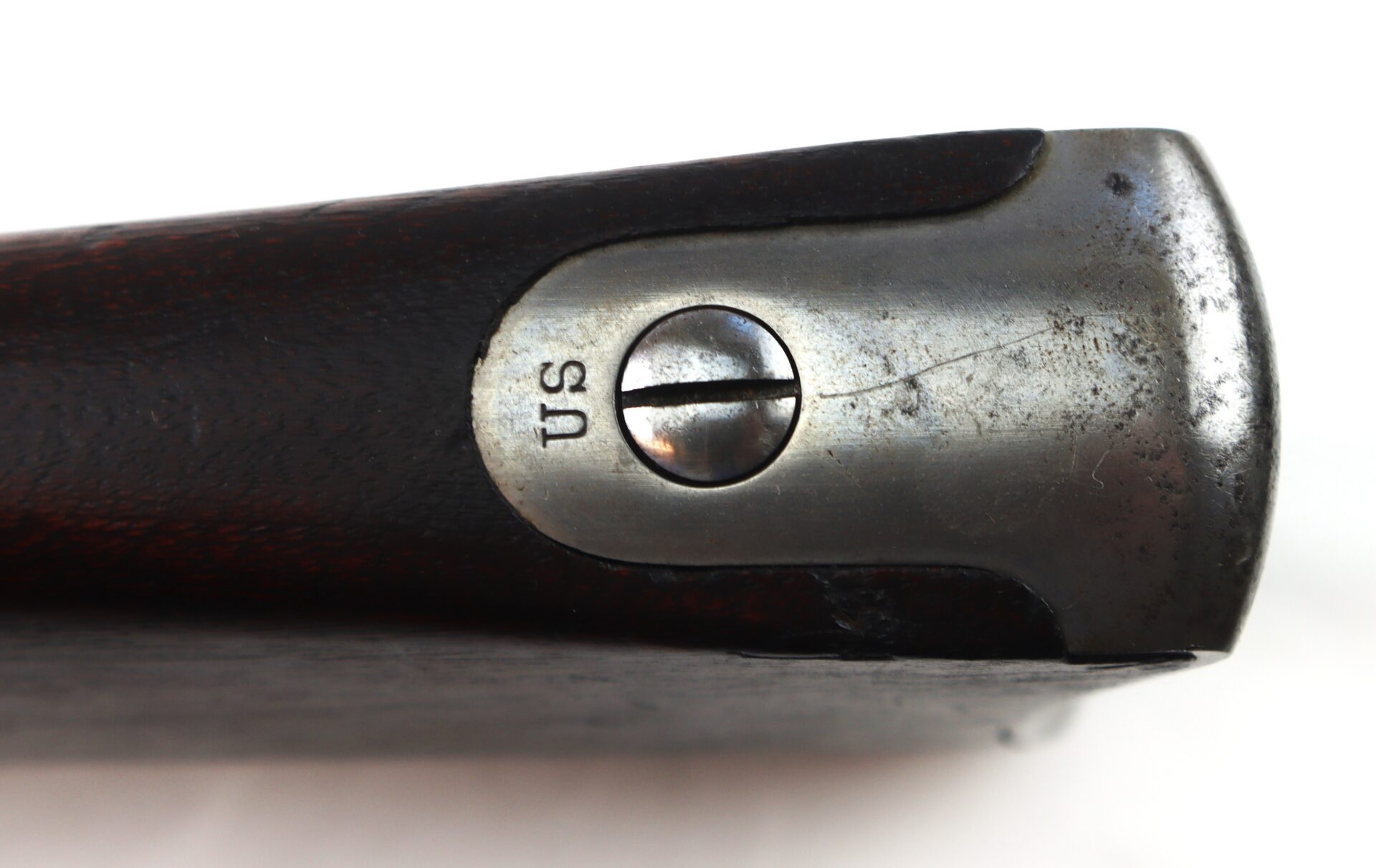 Close-up of a metal buttplate with a flathead screw and "US" engraved on it, attached to the dark wooden stock of a firearm.