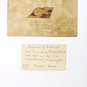 A Revolutionary War Flag Fragment with Exceptional 1883 Provenance is mounted on paper, featuring handwritten notes that identify it as a relic preserved in the War Department, Washington.