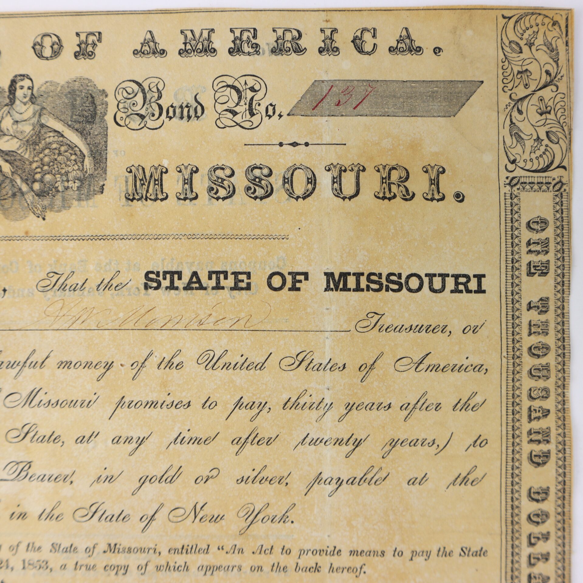 Close-up of an old Missouri bond certificate showing ornate text, a handwritten bond number, and part of an illustration in the upper left corner.