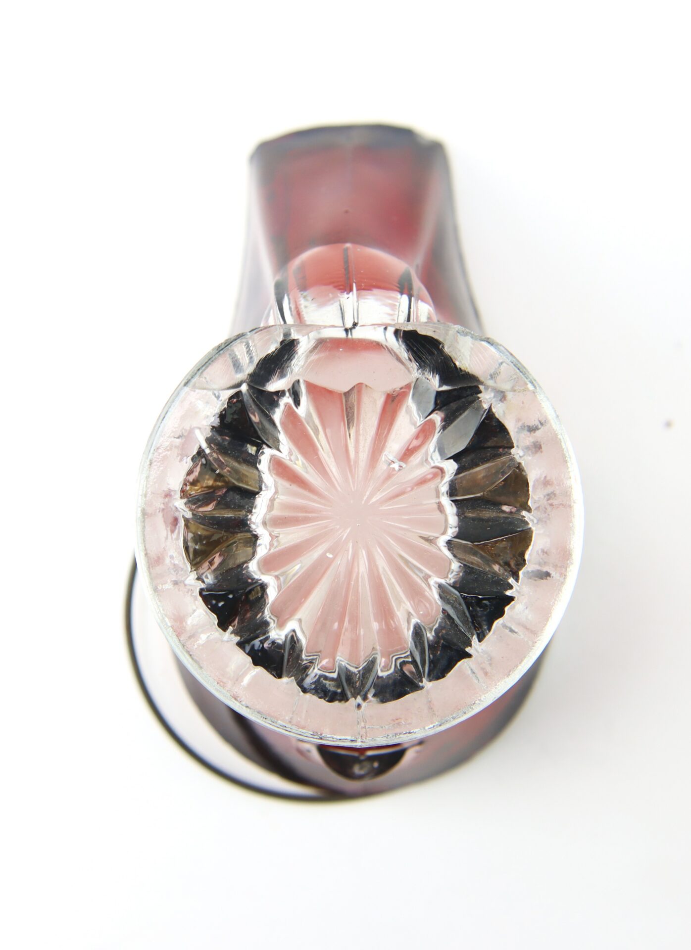 A clear glass with a starburst pattern on the base, viewed from above, with a dark red liquid inside, set against a white background.