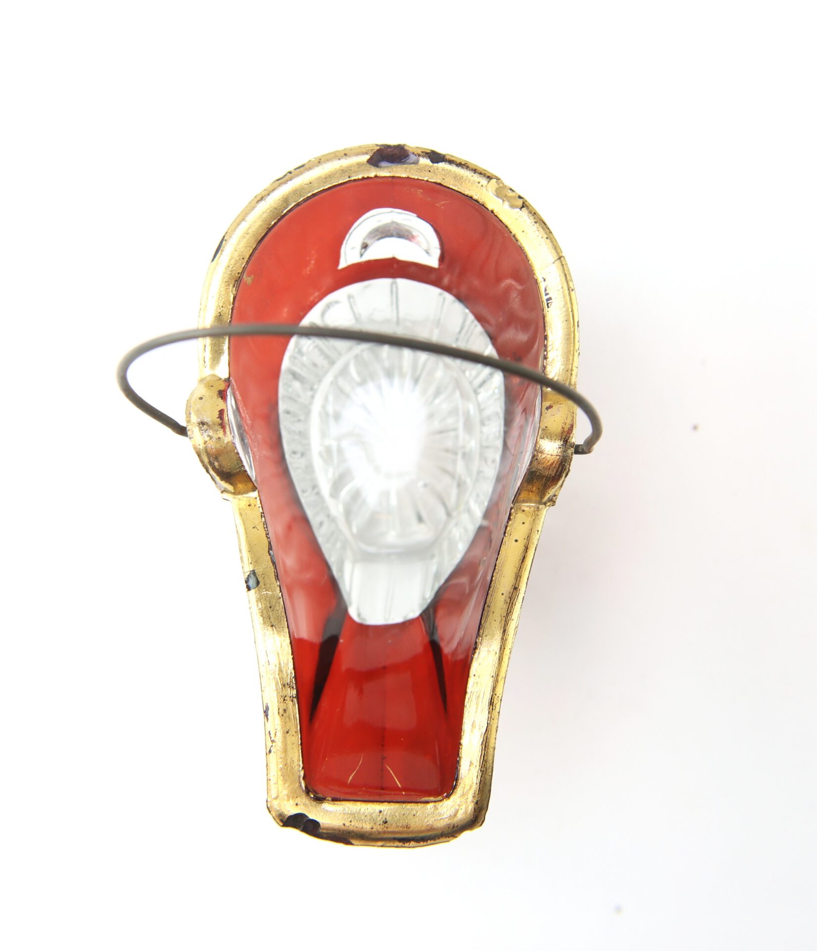 Overhead view of a vintage red and gold Christmas tree ornament with clear decorative detailing and a thin metal wire hook attached.