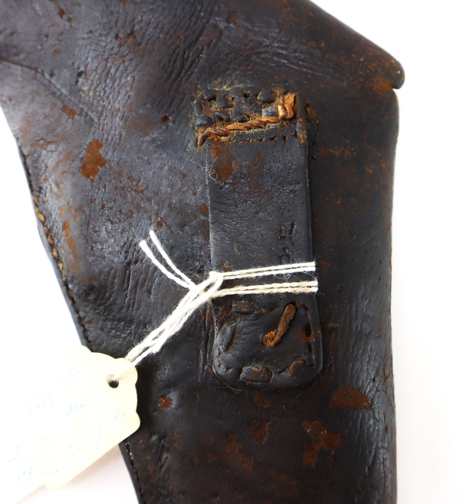 Close-up of an old, worn leather object with stitching, a rectangular patch, and a string-tied paper tag attached.