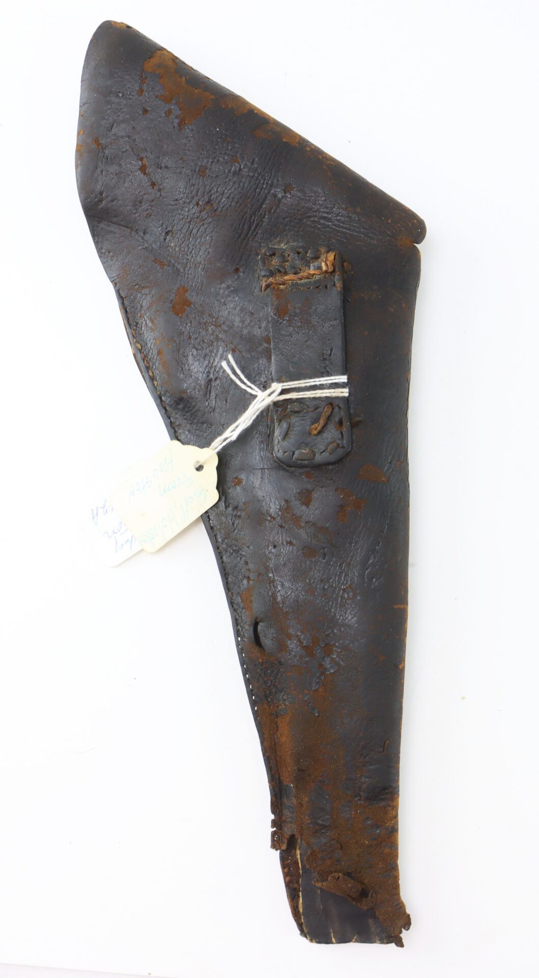 A worn, dark brown leather holster with visible cracks and rust marks, featuring a stitched belt loop and a white tag attached by string.