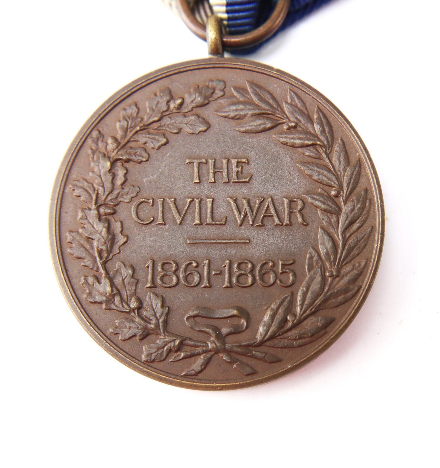 A bronze medal with a laurel and oak wreath, inscribed “THE CIVIL WAR 1861-1865,” attached to a blue and white striped ribbon.