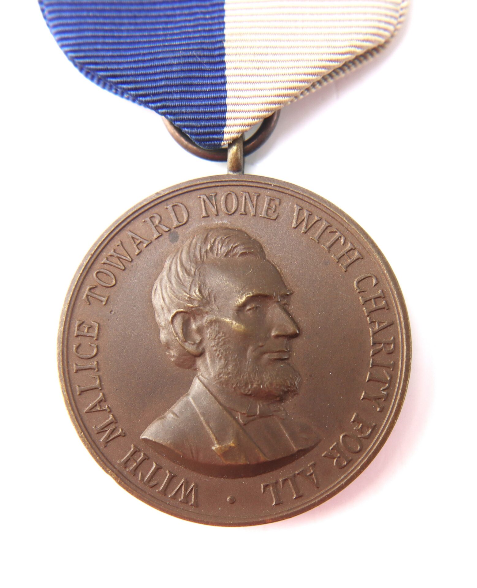 Bronze medal featuring Abraham Lincoln’s profile and the text “WITH MALICE TOWARD NONE WITH CHARITY FOR ALL,” attached to a blue and white ribbon.