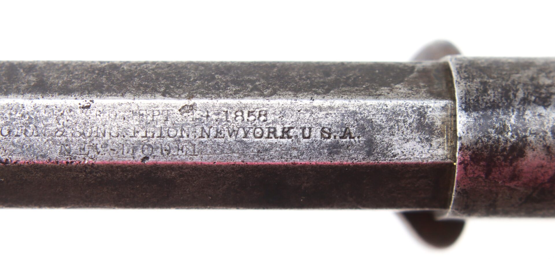 Close-up of an old metal object with engraved text reading “NEW YORK U.S.A.” and “1855,” showing signs of age and wear.