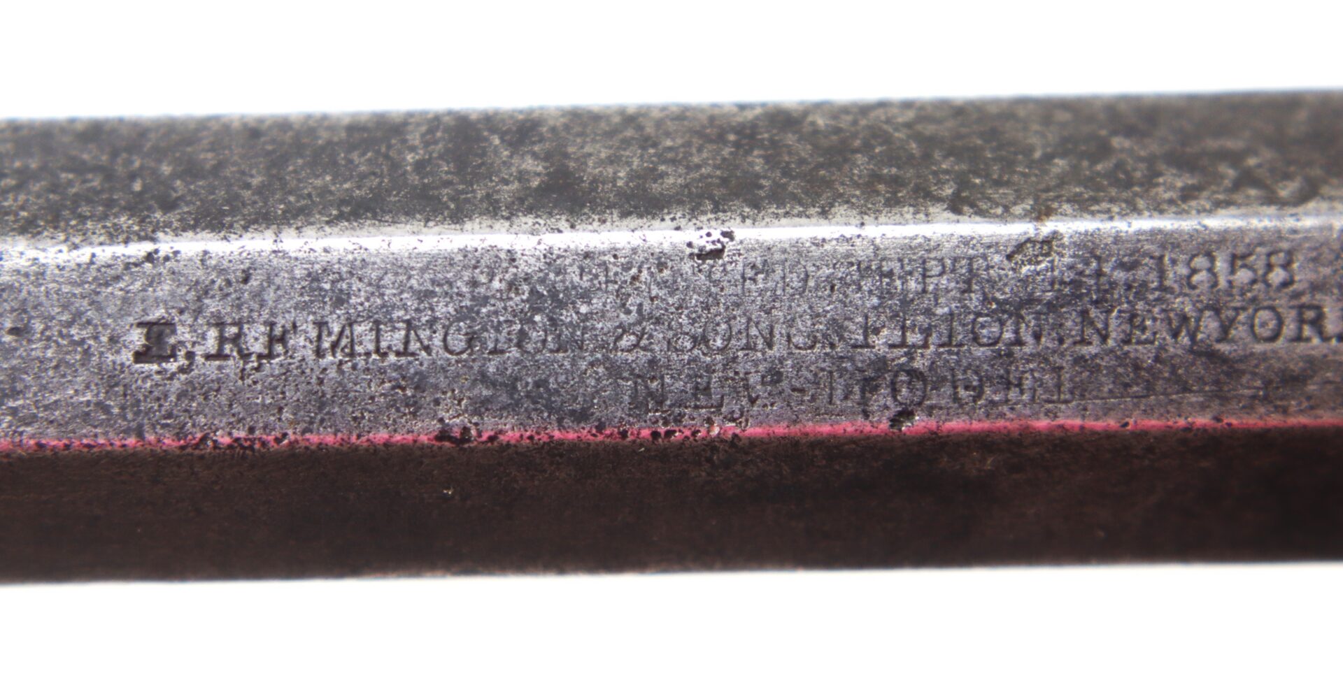 Close-up of a metal surface with worn, partially legible engraved text; “Remington” and “New York” are faintly visible.