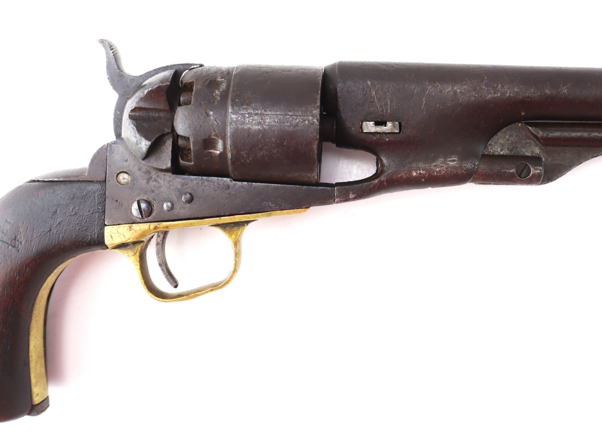 Close-up of an antique revolver with a wooden grip, brass trigger guard, and visible hammer and cylinder, photographed on a white background.