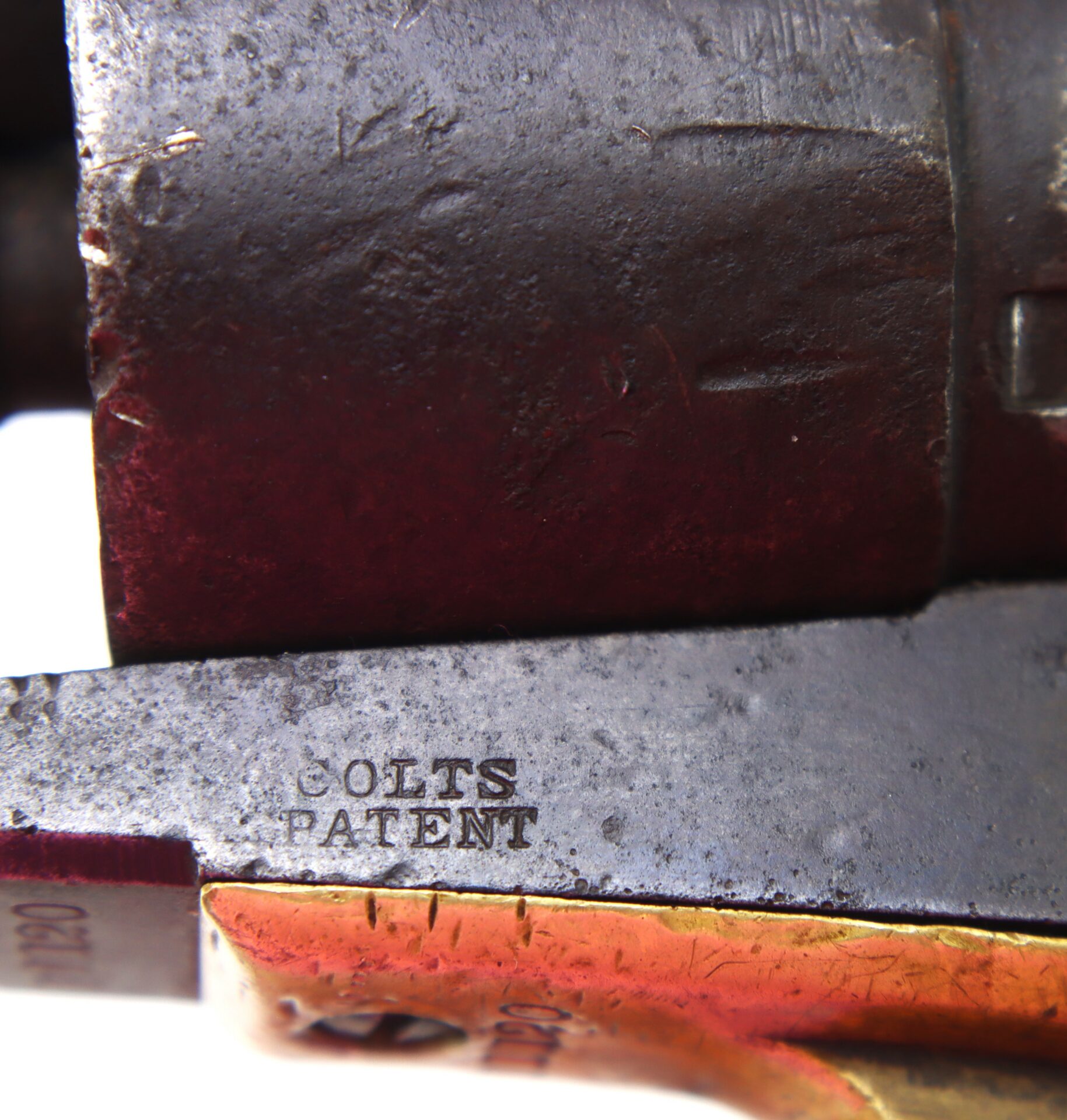 Close-up of a metal object with engraved text reading “COLTS PATENT,” showing weathered and worn surfaces.
